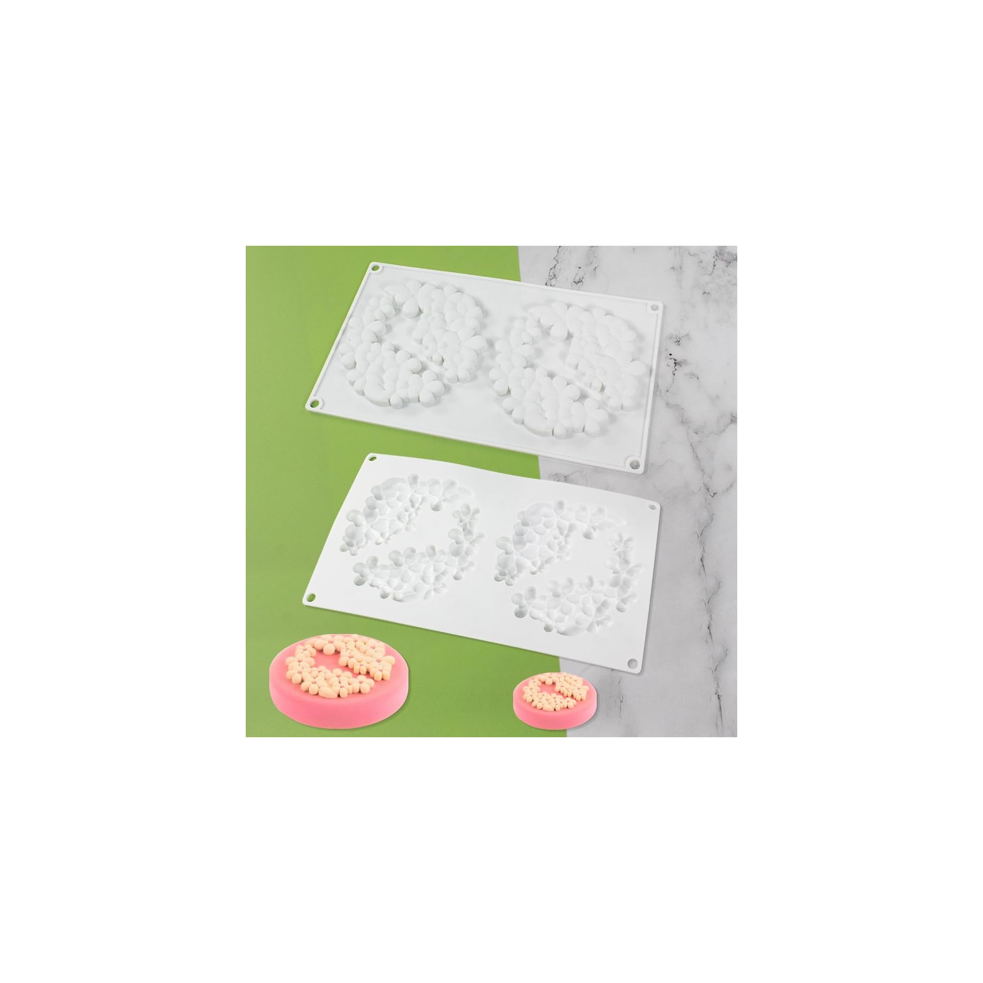 Zwei weiße Silikonformen und zwei rosa Kuchen mit weißer Blütendekoration.