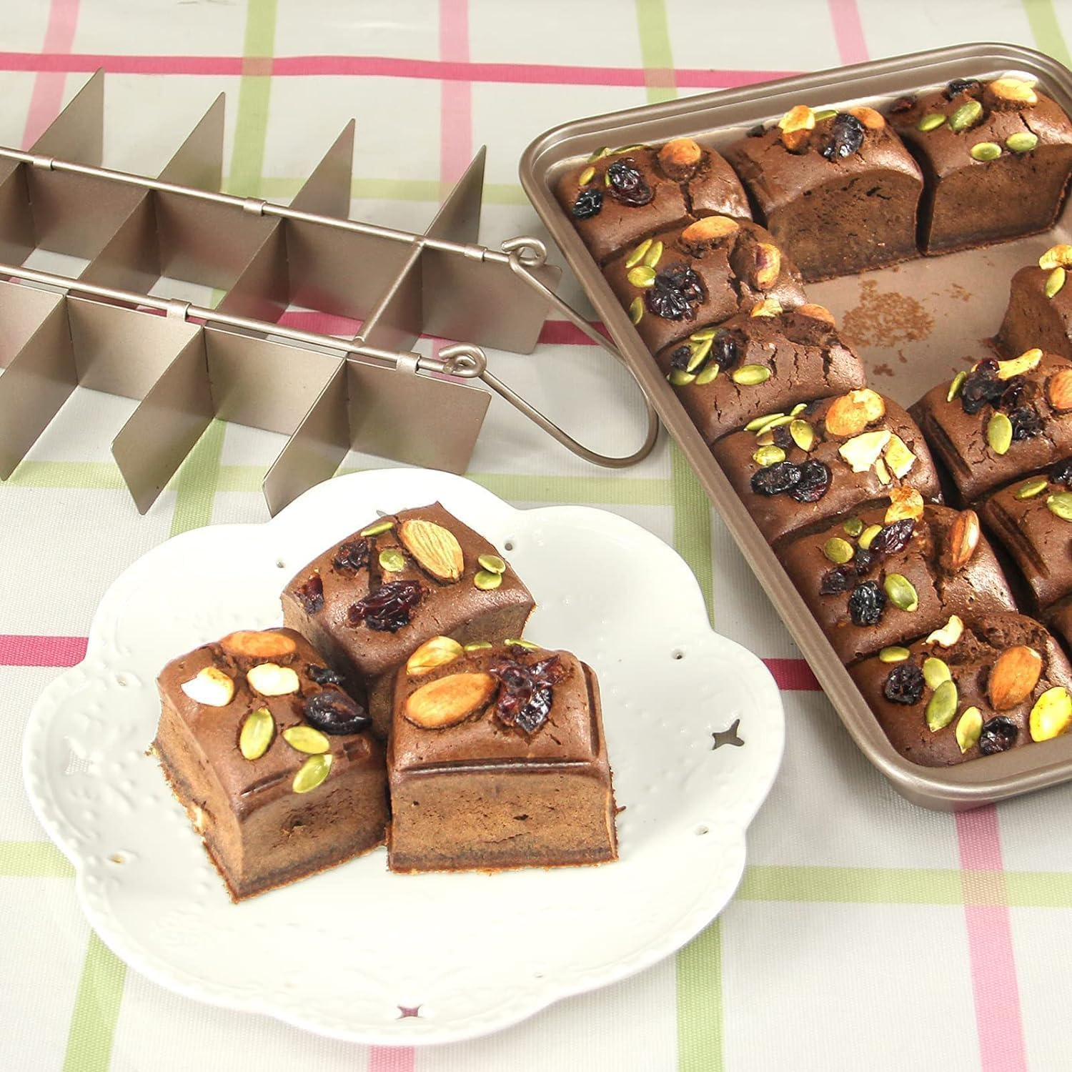 Schokoladenkuchenstücke mit Mandeln und Beeren in einer Backform, ein Teiler und drei Stücke auf einem Teller.