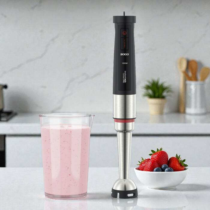 Un frullatore a immersione nero e argento accanto a un bicchiere di smoothie rosa e bacche fresche.
