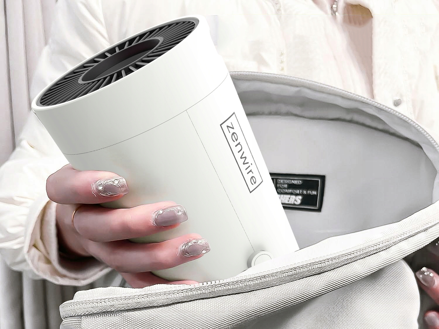 Persona che ripone un mini ventilatore Zenwire bianco in una borsa aperta.