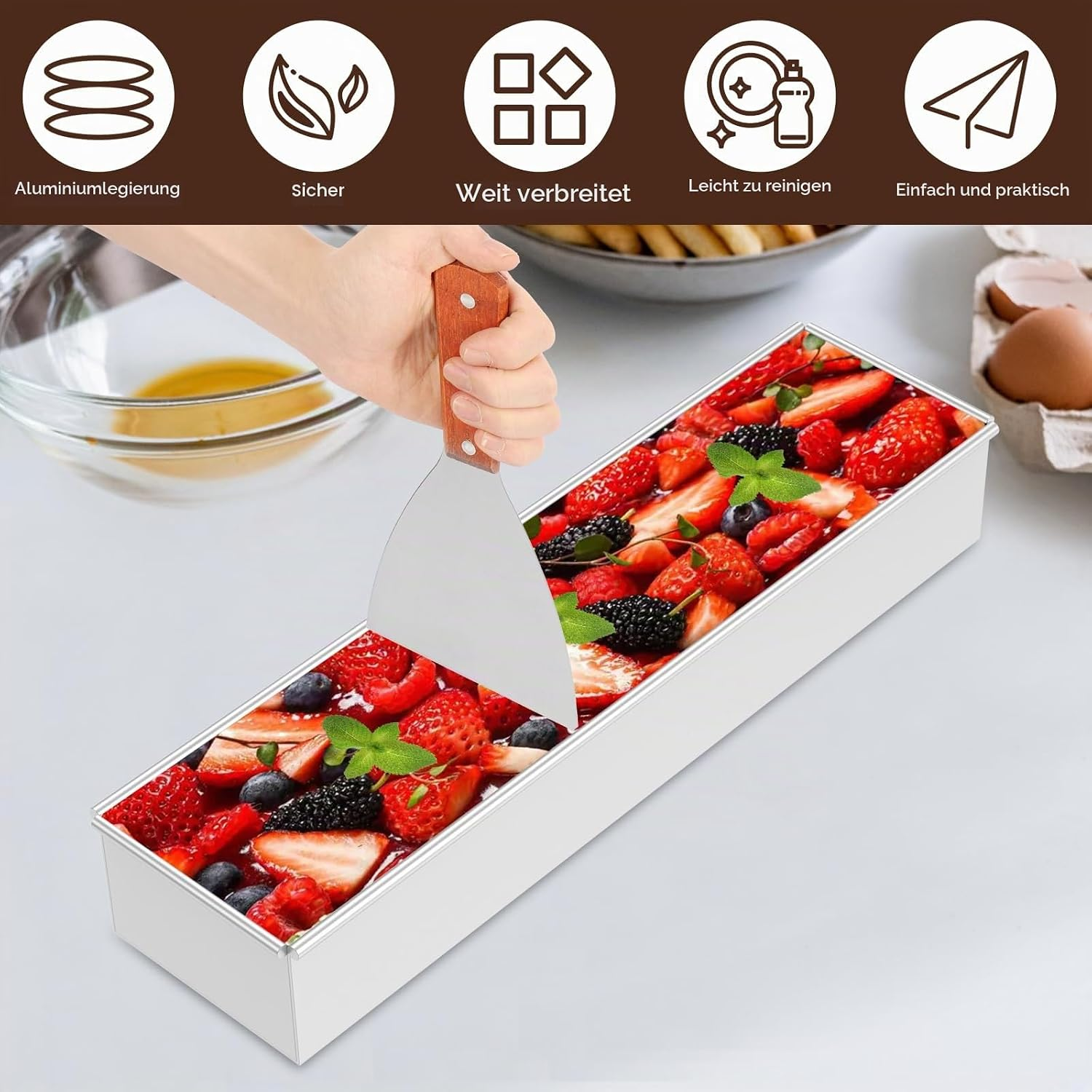 Eine Hand schneidet mit einem Spatel eine Beeren-Torte in einer rechteckigen Metallbackform.