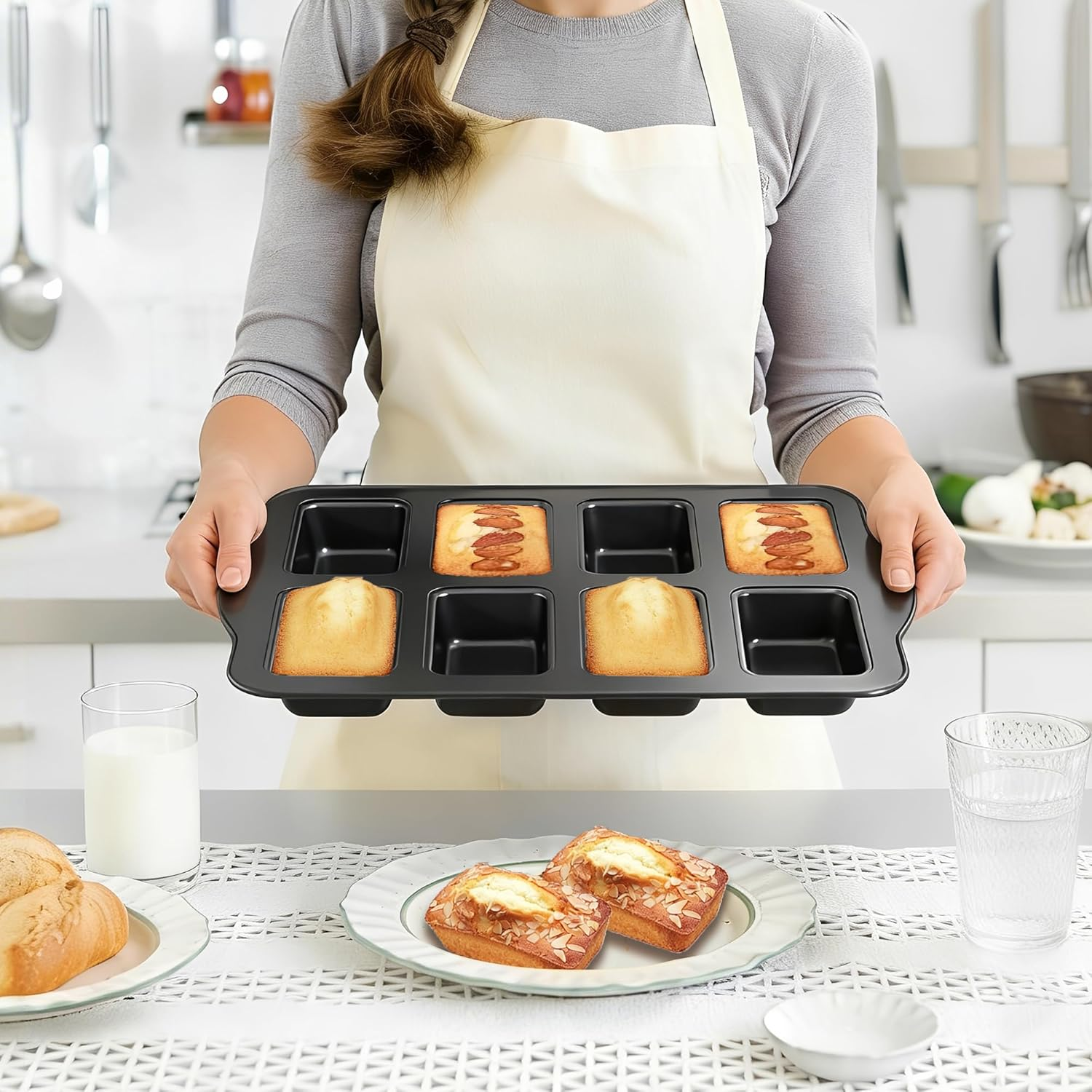 Eine Person im Apron hält eine Backform mit Kuchen, während auf dem Tisch Gebäck und Gläser stehen.