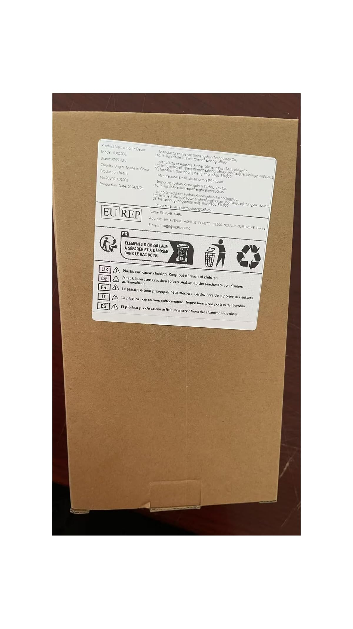 Ein brauner Karton zeigt ein weißes Produktetikett mit Text, Recyclingsymbolen und Sicherheitshinweisen.