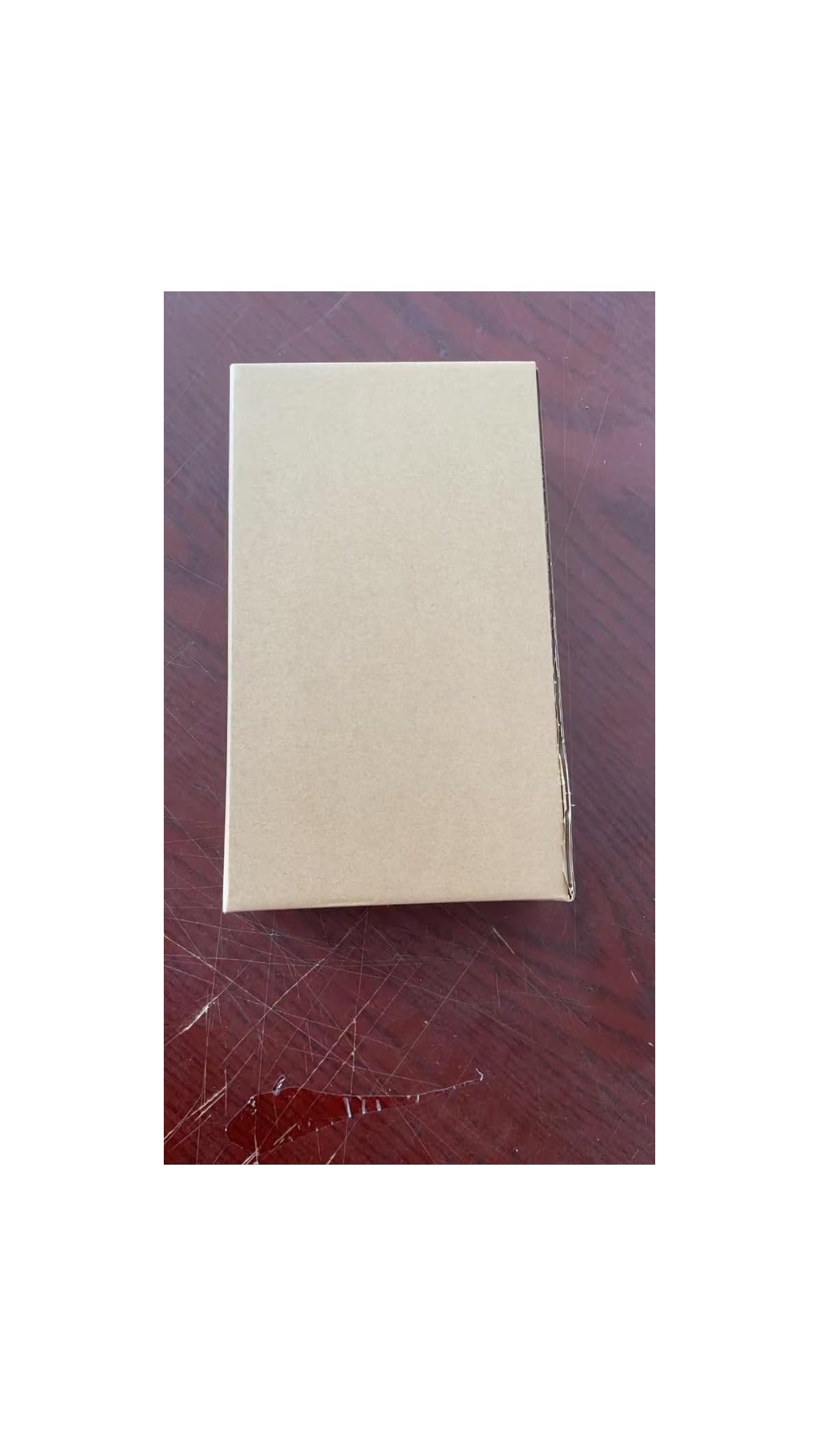 Eine rechteckige braune Pappschachtel liegt auf einer dunkel verkratzten Holzoberfläche.