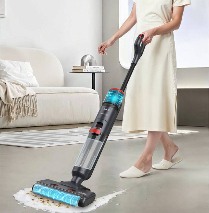 Una donna in abito beige usa un aspirapolvere lavapavimenti senza fili su un pavimento grigio.
