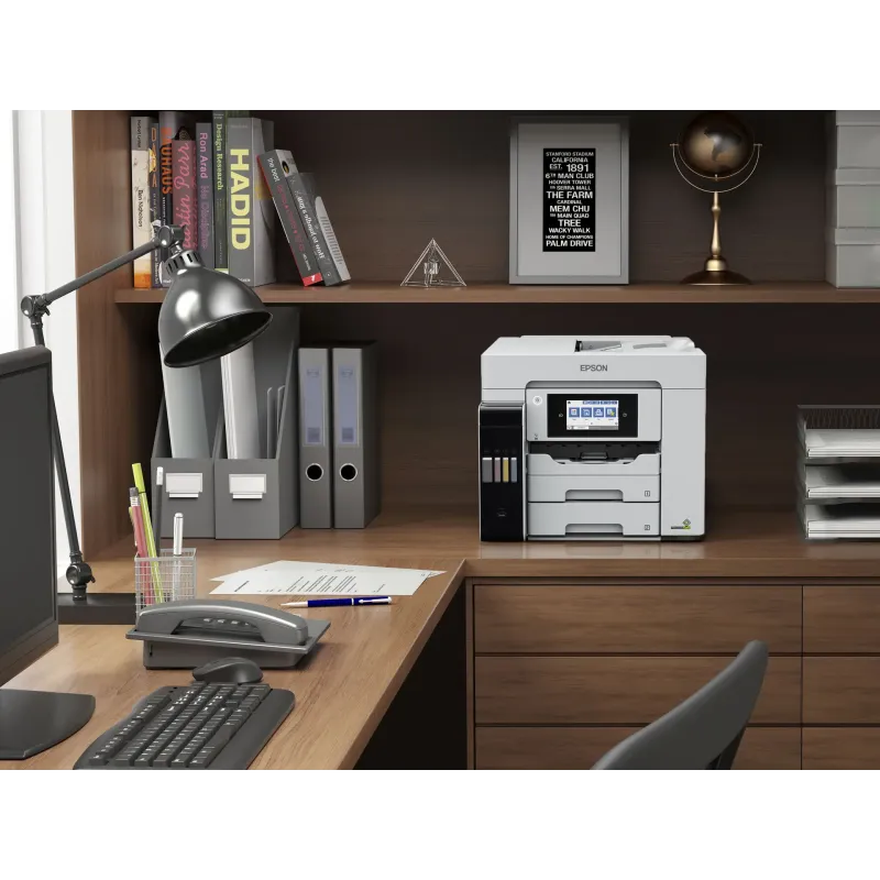 Un bureau bien rangé avec une imprimante Epson blanche, un ordinateur, une lampe et des étagères remplies de livres.