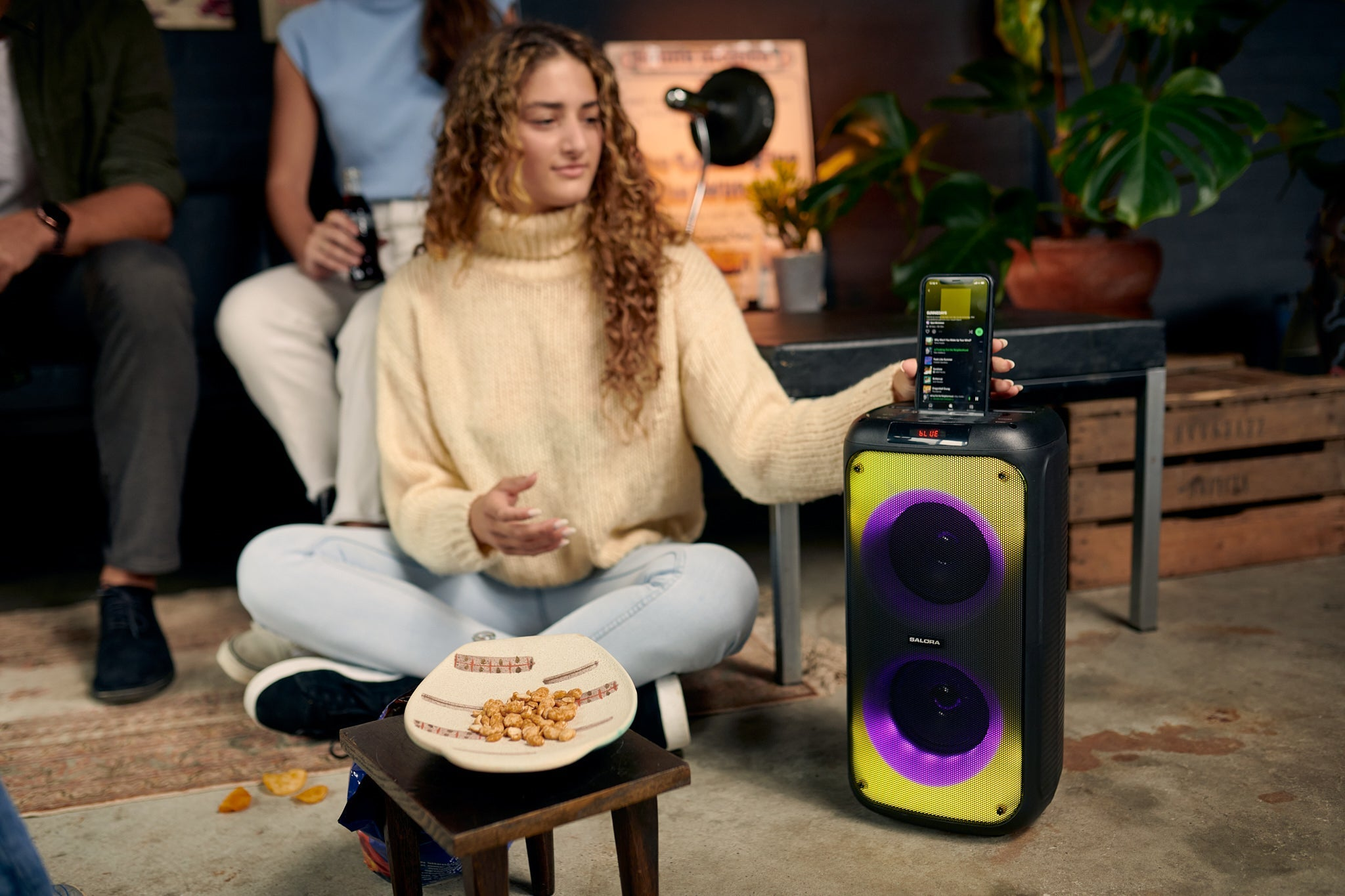 Eine blonde Frau sitzt auf dem Boden und verbindet ein Smartphone mit einem großen Bluetooth-Lautsprecher.