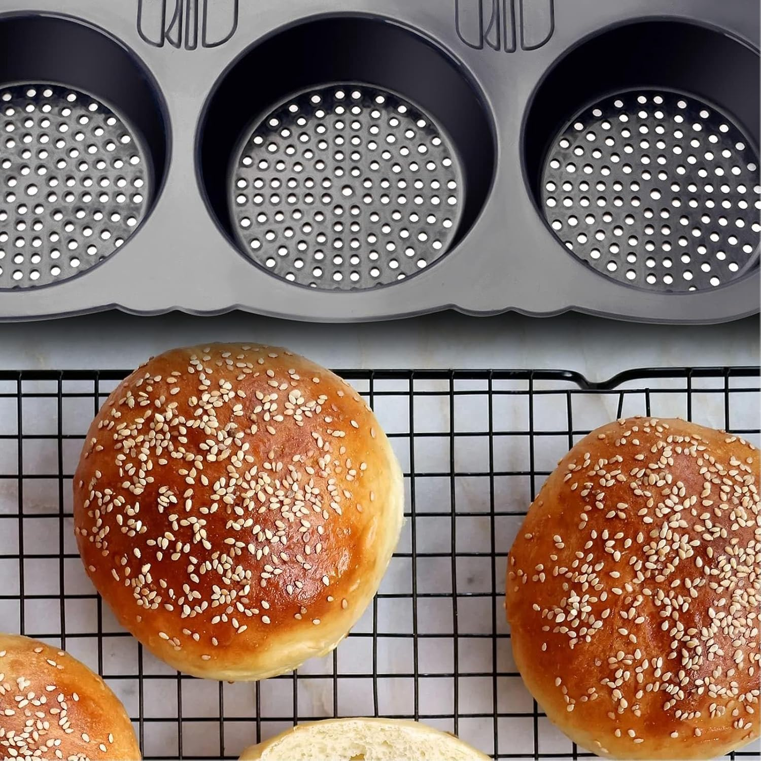 Graue Muffinbackform mit Löchern oben und Sesambrötchen auf einem Kühlgitter unten.