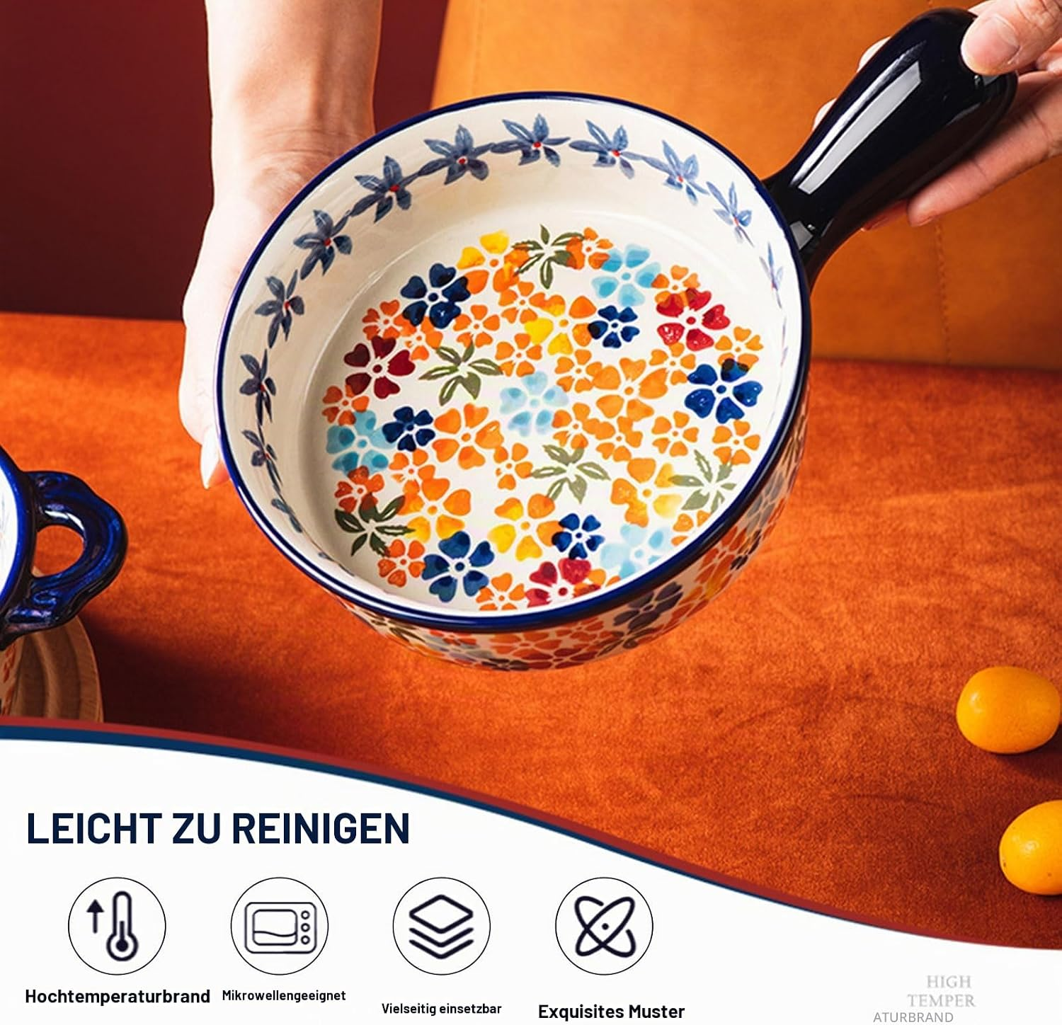 Eine Hand hält eine weiße Keramikschüssel mit buntem Blumenmuster und blauem Griff über einem orangen Tisch.