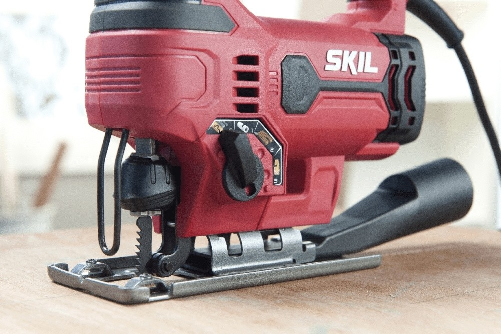 Siyah saplı ve gümüş metal tabanlı kırmızı bir Skil dekupaj testeresi ahşap masa üzerinde duruyor.