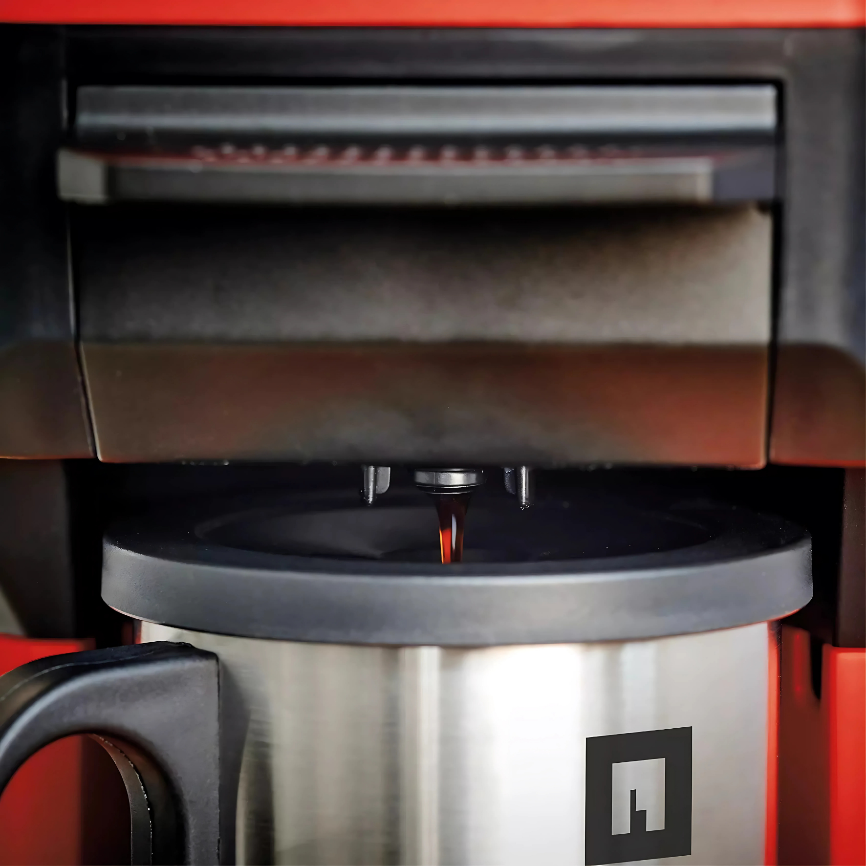 Il caffè fuoriesce da una macchina rossa e nera in una tazza termica.