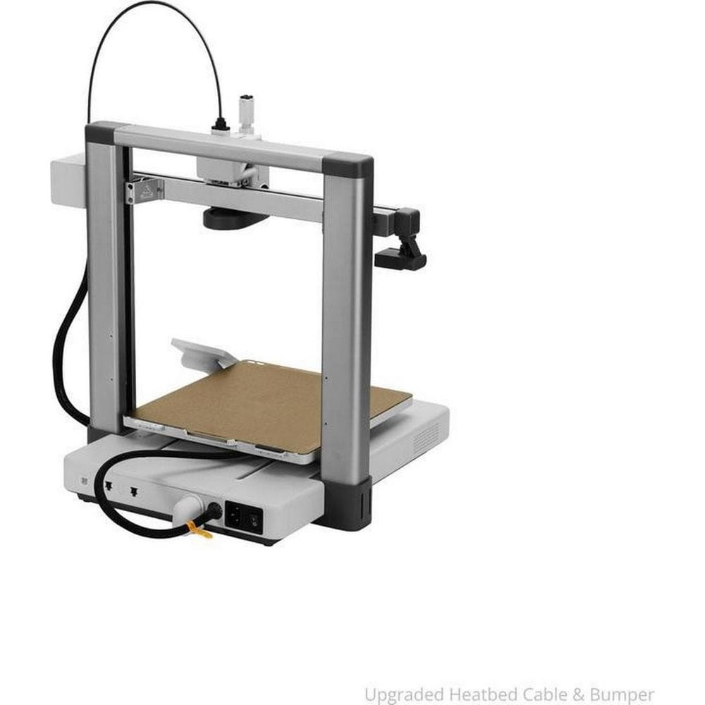 Una stampante 3D argentata con piatto riscaldato e cavi su sfondo bianco.
