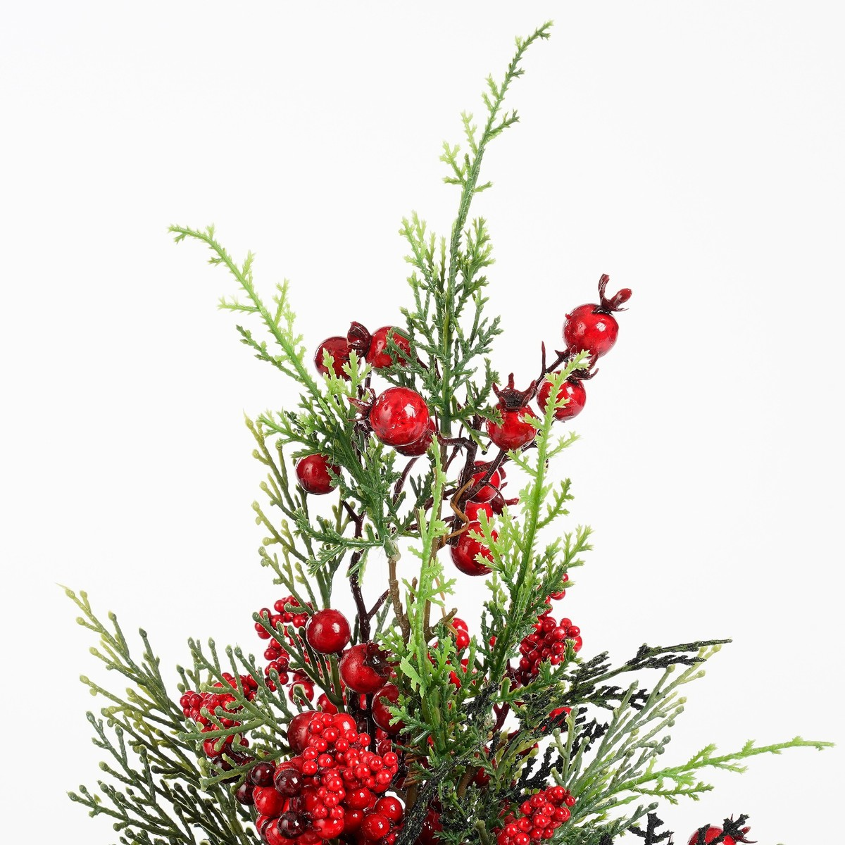 Branche de sapin de Noël artificielle avec des aiguilles vertes et des baies rouges sur fond blanc.