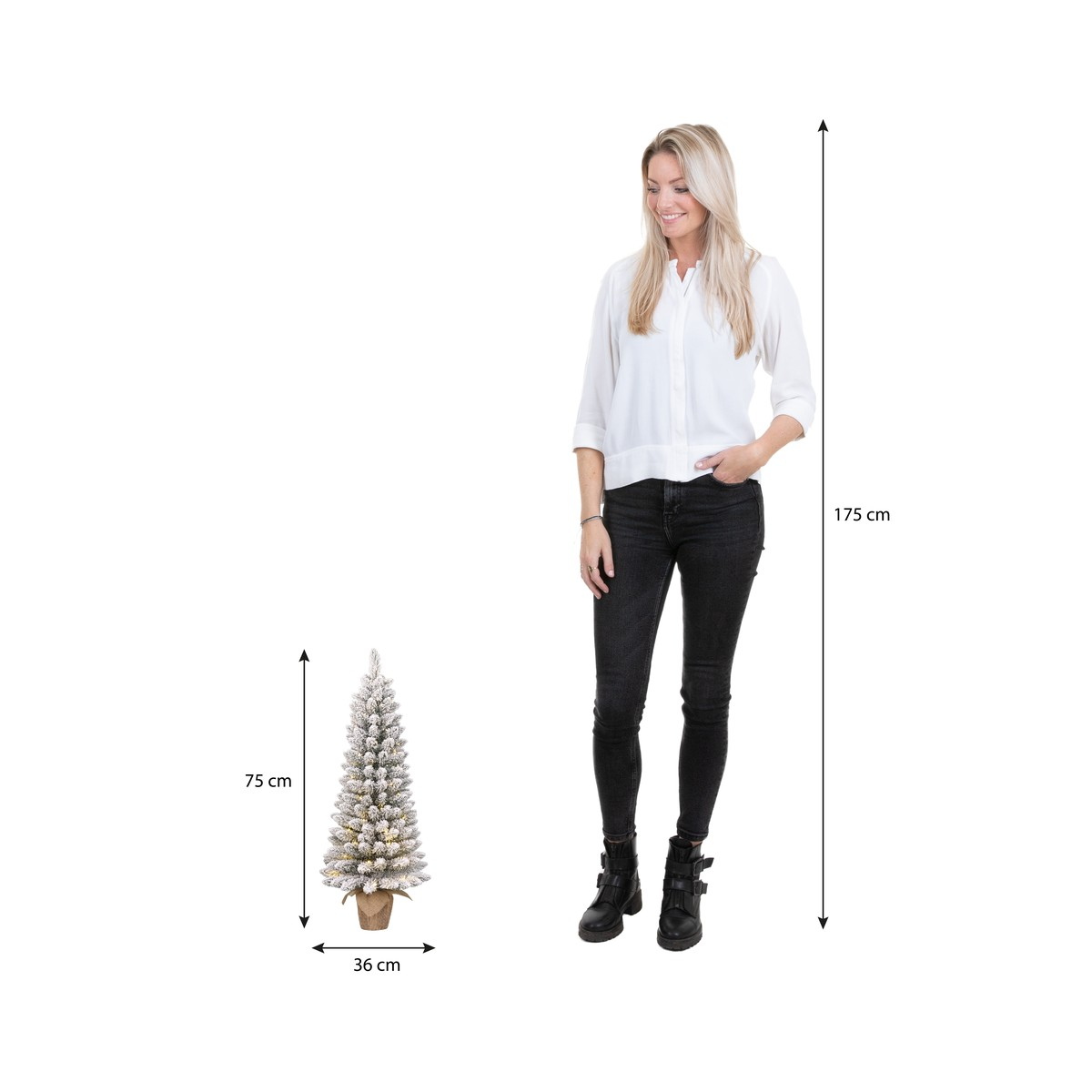 Een vrouw in witte blouse en zwarte jeans staat naast een kunstkerstboom van 75 cm hoog.