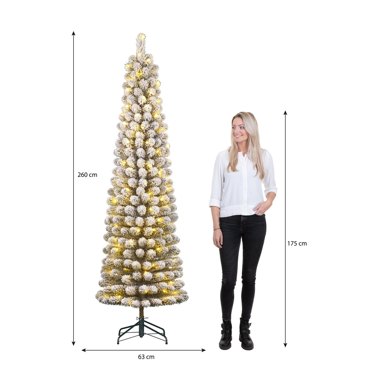 Een vrouw staat naast een hoge, besneeuwde kunstkerstboom met lampjes en afmetingen.
