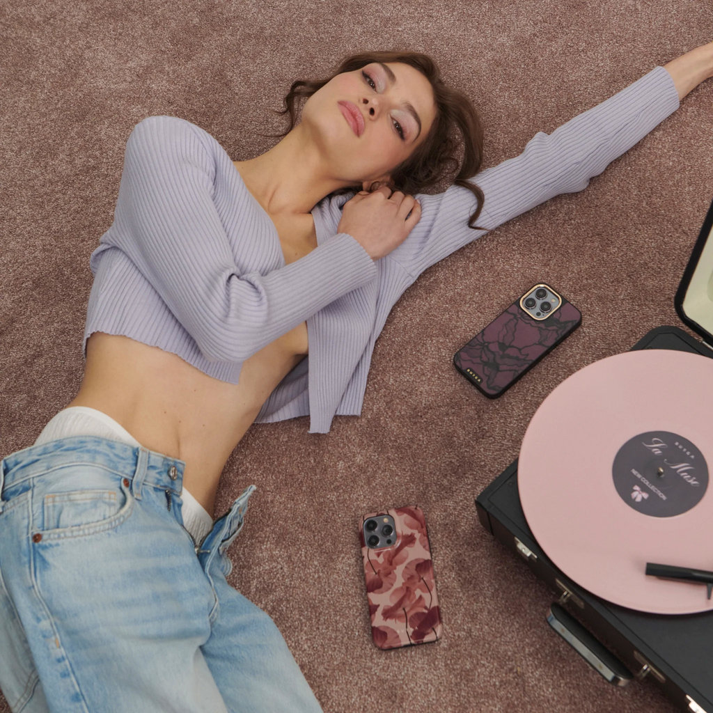 Une femme en gilet lavande et jean est allongée sur un tapis marron près de téléphones et d'un tourne-disque.
