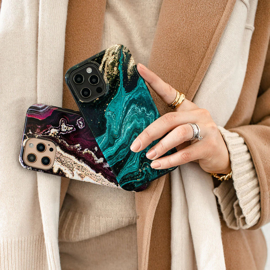 Une personne en manteau beige tient deux smartphones avec des coques en marbre.