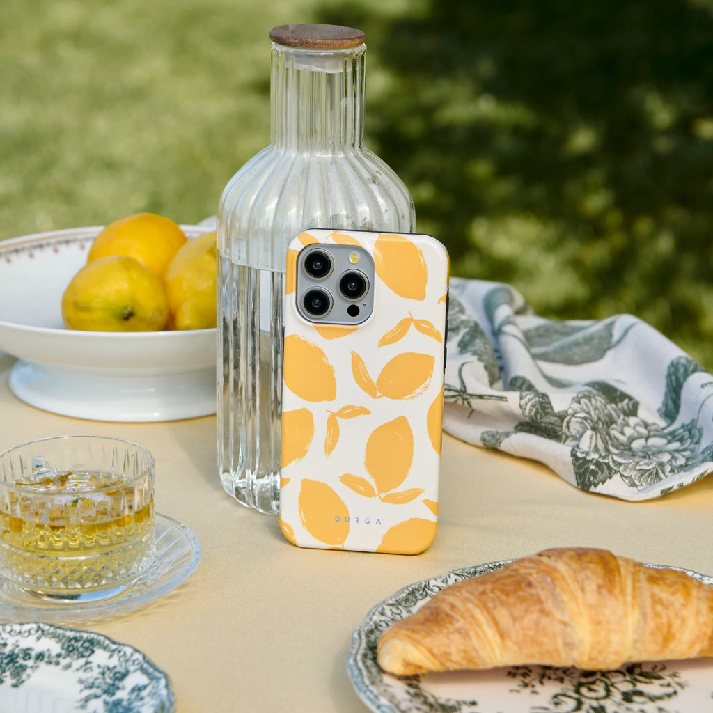 Coque de téléphone motif citron sur une table avec carafe d'eau, tasse de thé, croissant et citrons.