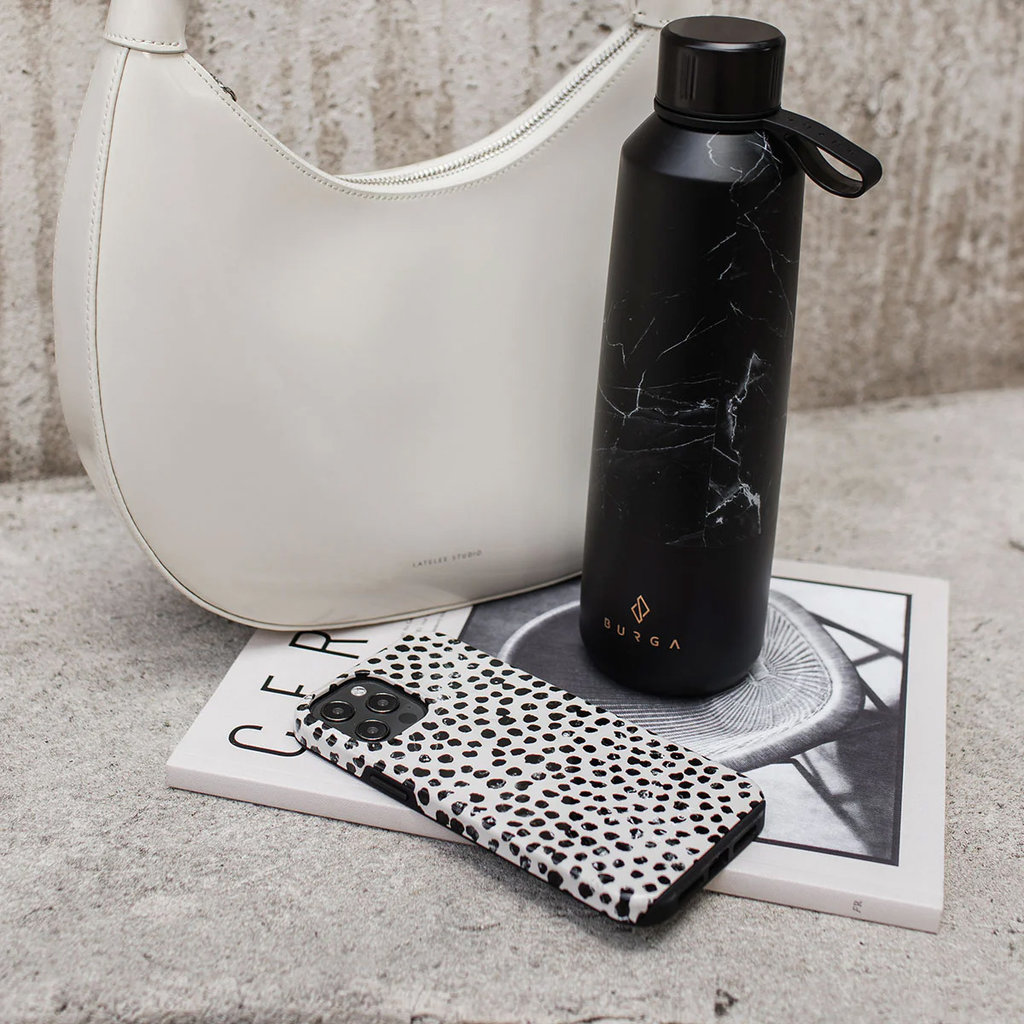 Sac blanc, bouteille marbre noir et coque noir et blanc sur livre devant béton.