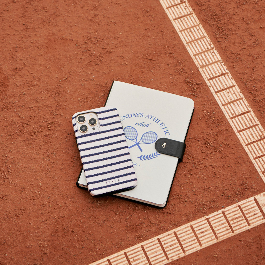 Een blauw-wit gestreepte telefoon en een notitieboekje op een rode gravel tennisbaan naast een witte lijn.