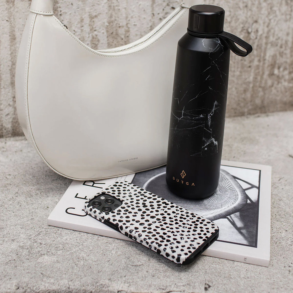 Une bouteille d'eau en marbre noir, un smartphone blanc à pois, un sac blanc et un magazine sur la pierre.