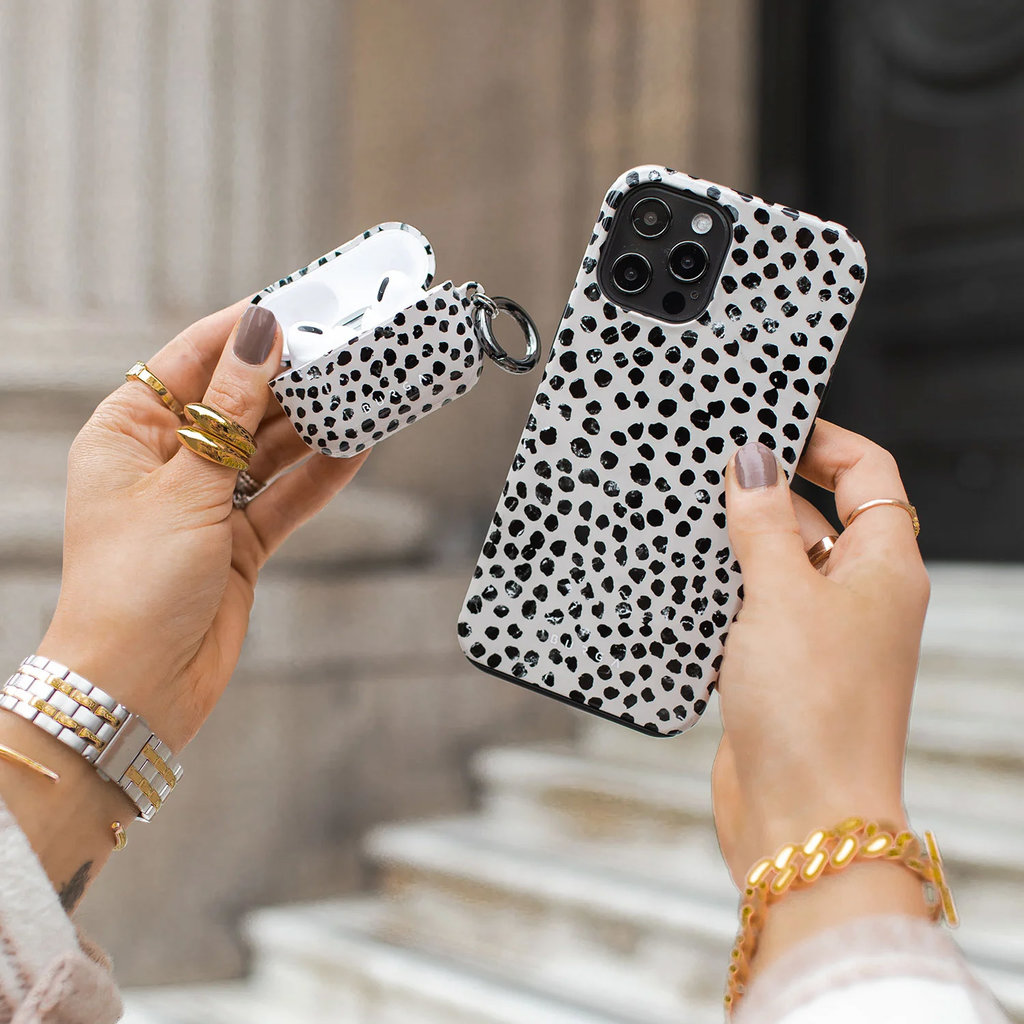 Personne tenant un téléphone et un étui AirPods avec un motif dalmatien noir et blanc.