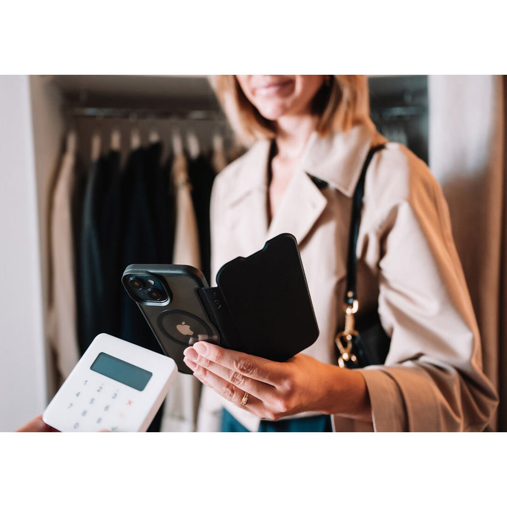 Una donna con giacca chiara tiene uno smartphone con custodia vicino a un POS in un negozio.