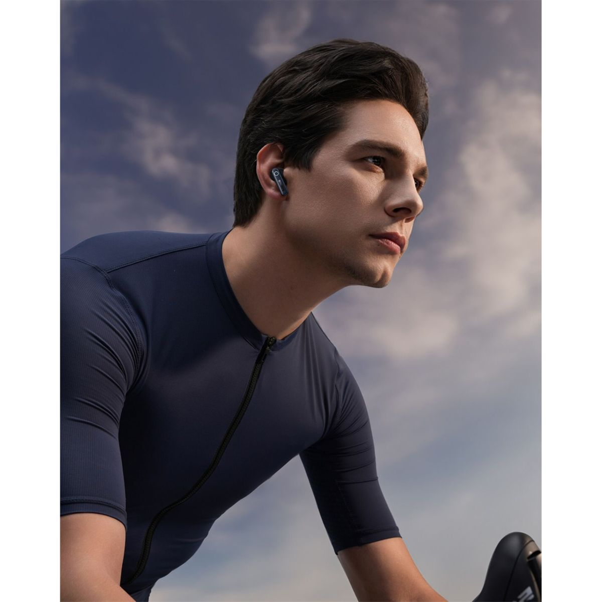 Ein Radfahrer mit schwarzem Trikot und Ohrhörern fährt unter einem bewölkten Himmel.