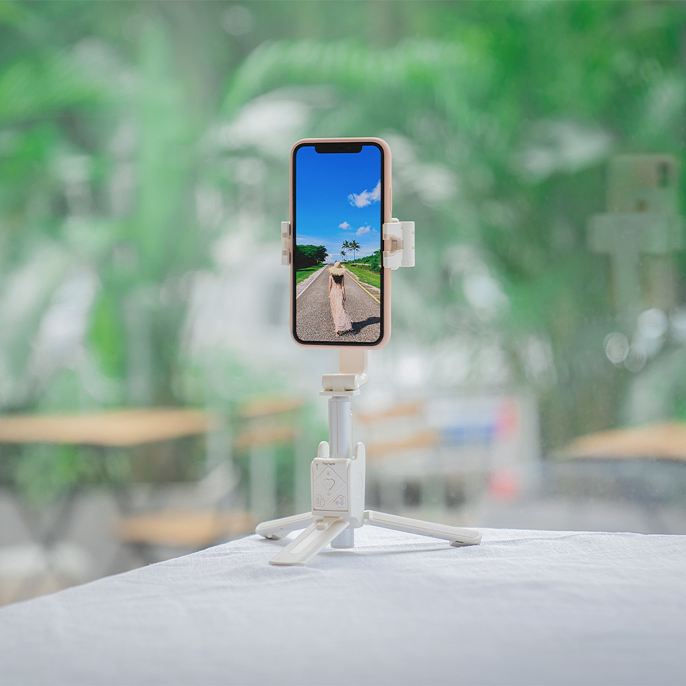 Ein Smartphone auf einem kleinen weißen Stativ auf einem Tisch vor verschwommenem Grün.