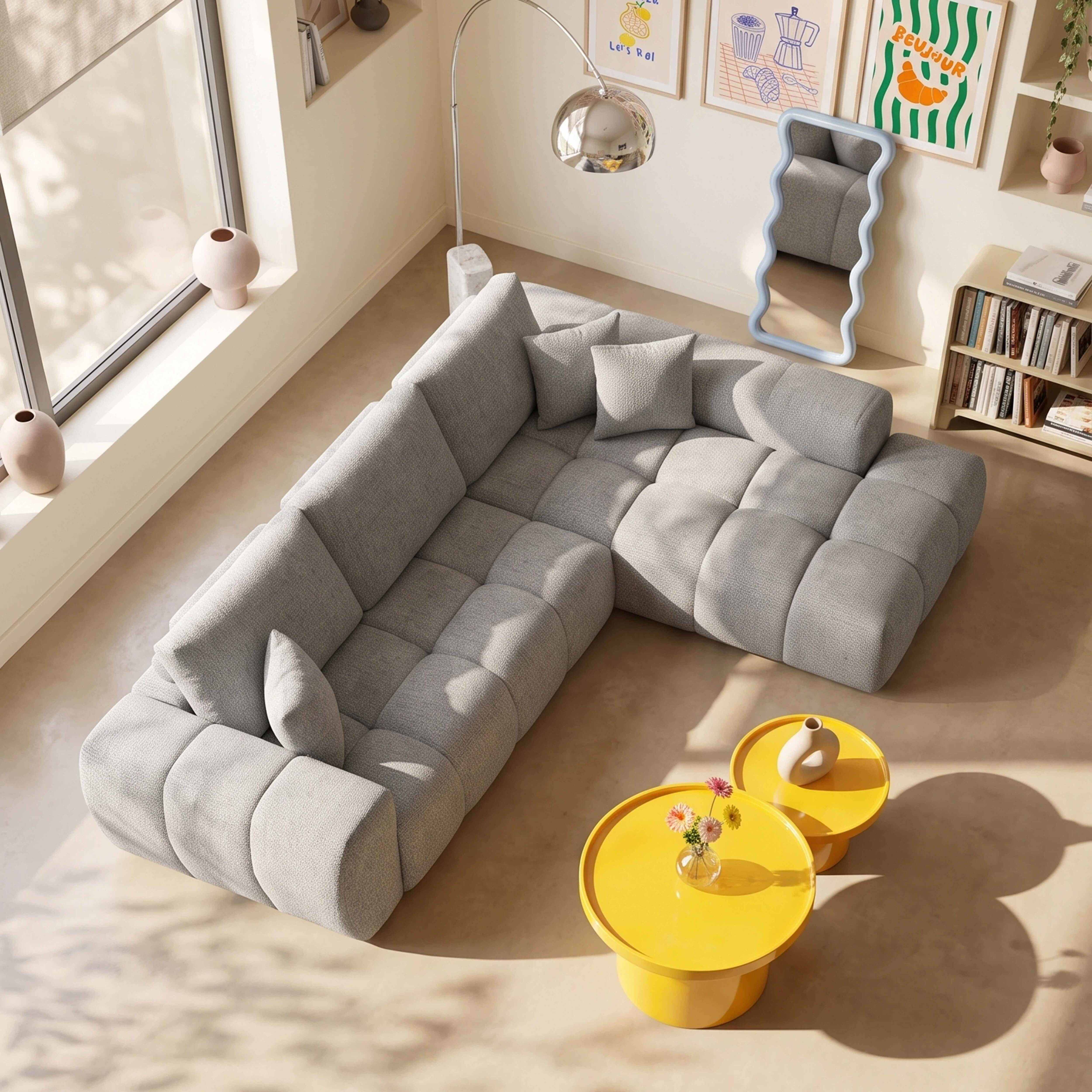 Draufsicht auf ein Wohnzimmer mit grauem Ecksofa, zwei gelben runden Tischen und einfallendem Sonnenlicht.