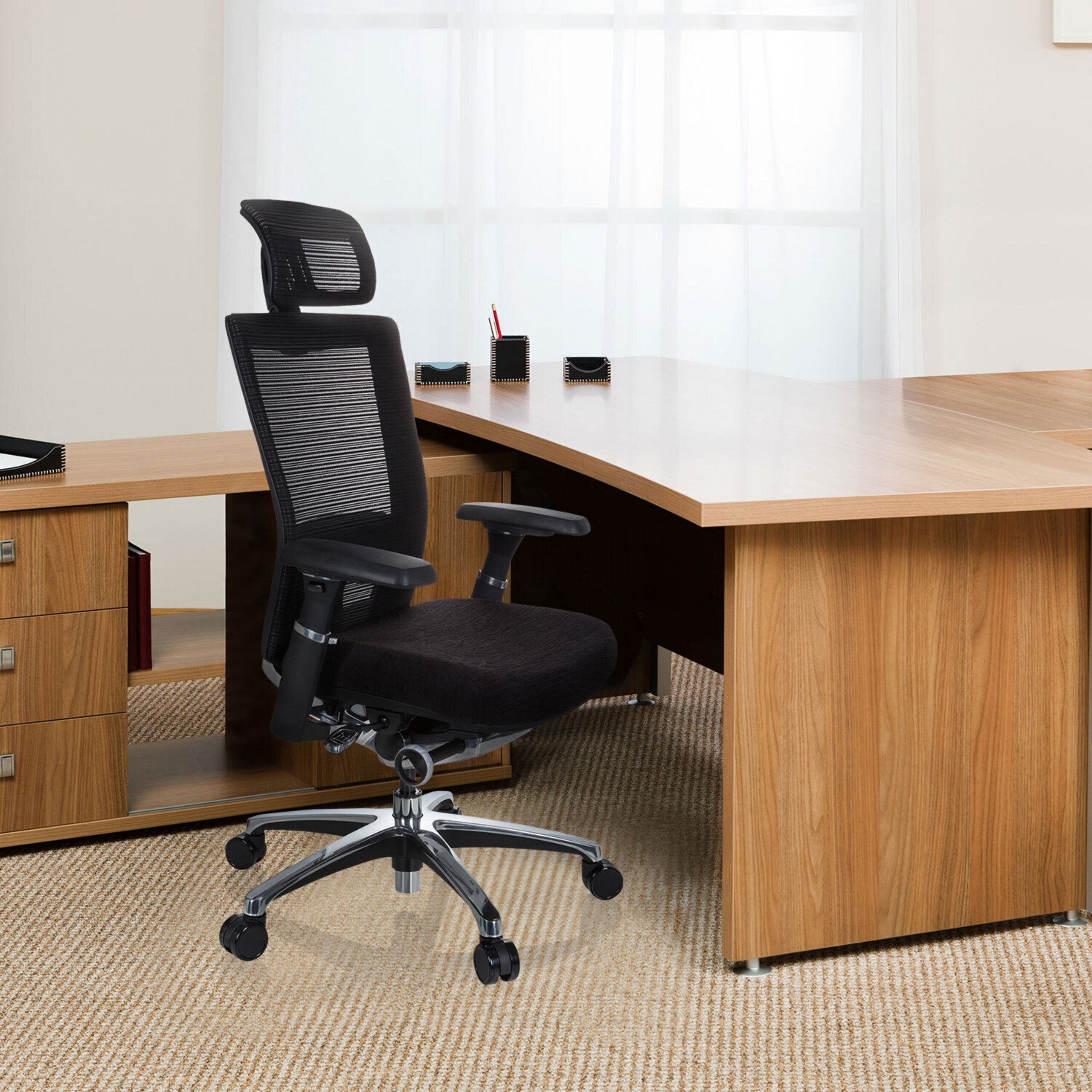 Ein schwarzer ergonomischer Buerostuhl steht vor einem Holztisch in einem hellen Raum.
