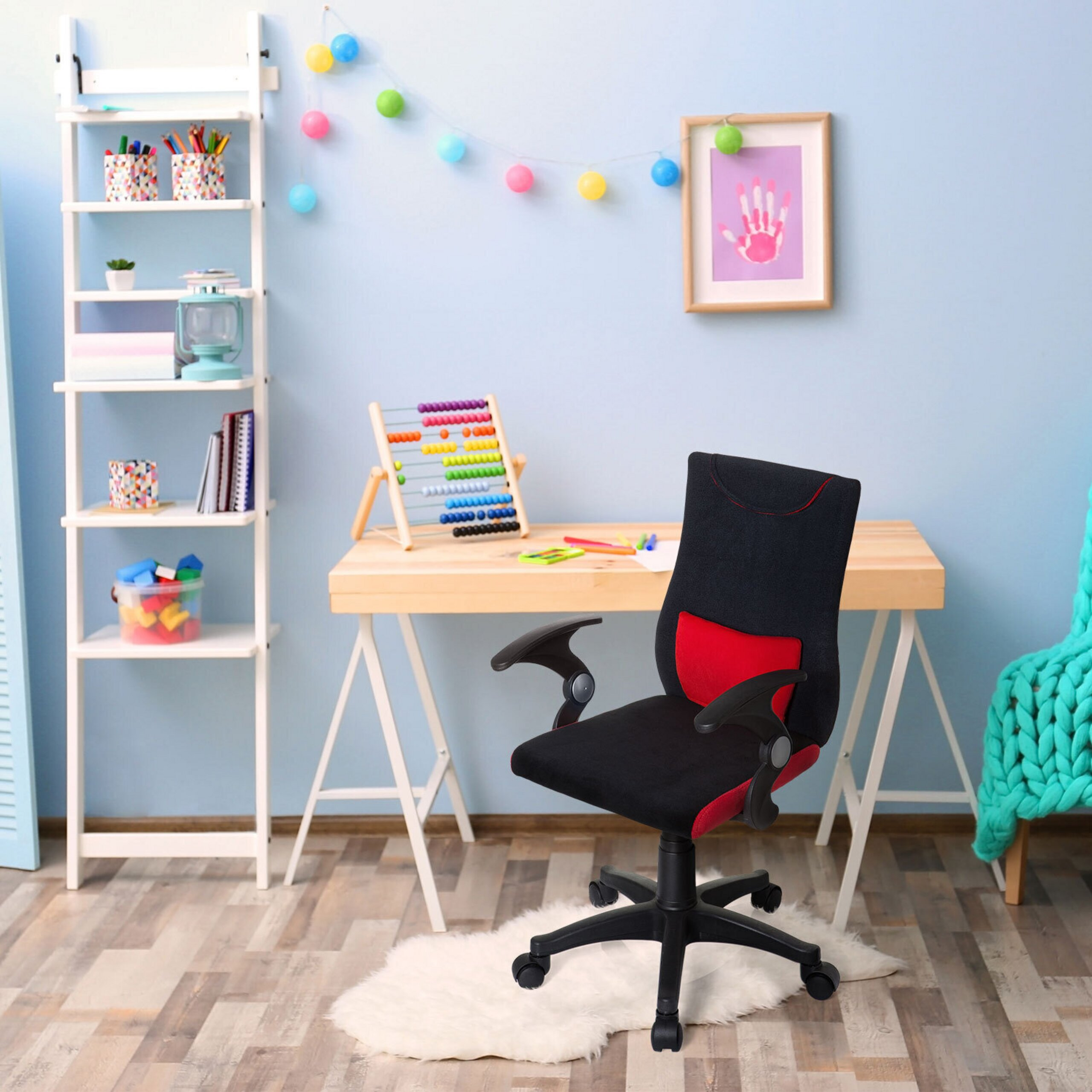 Ein schwarzer und roter Schreibtischstuhl steht vor einem Schreibtisch in einem bunten Kinderzimmer mit blauen Wänden.