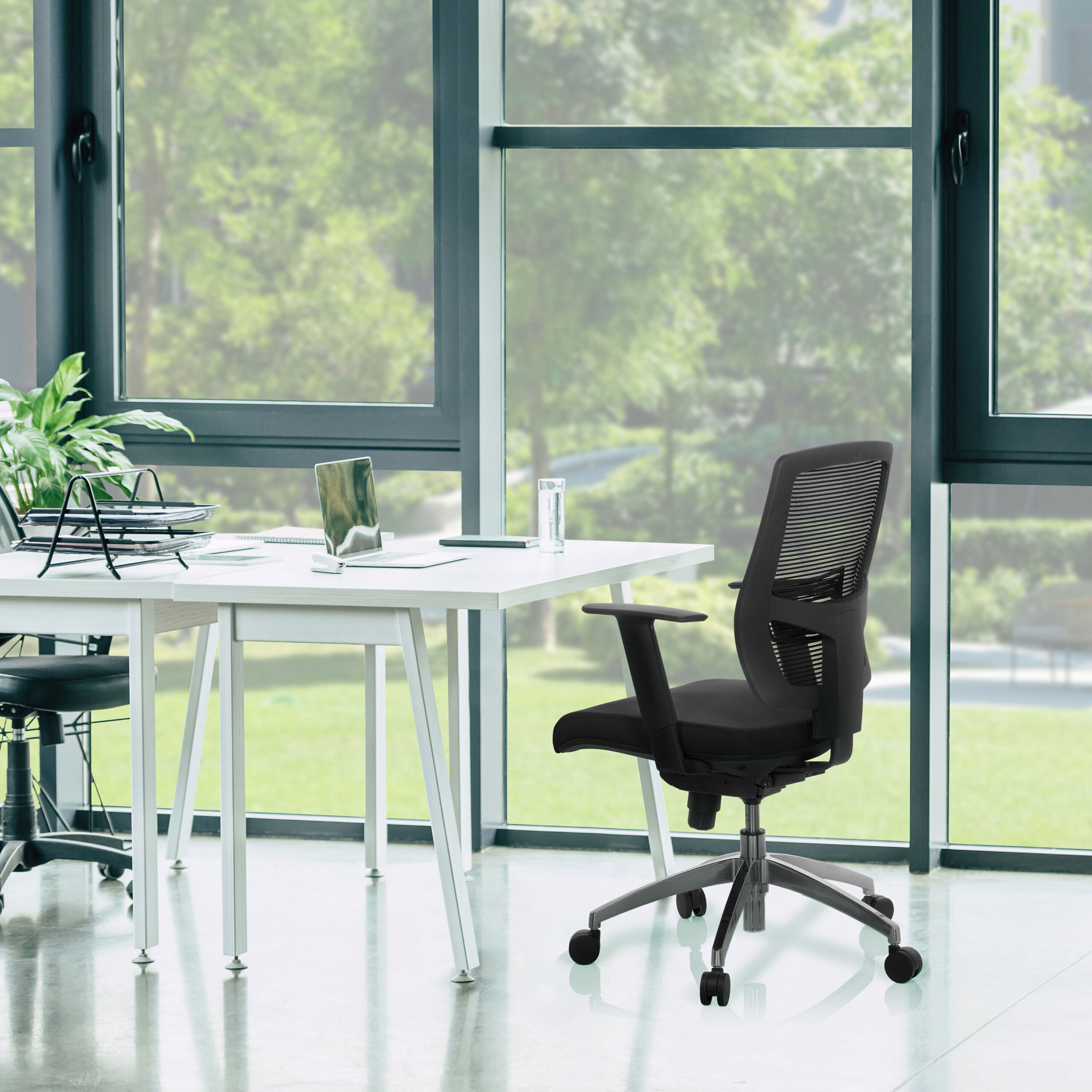 Ein modernes Büro mit schwarzem Mesh-Bürostuhl, weißem Schreibtisch mit Laptop und großen Fenstern.