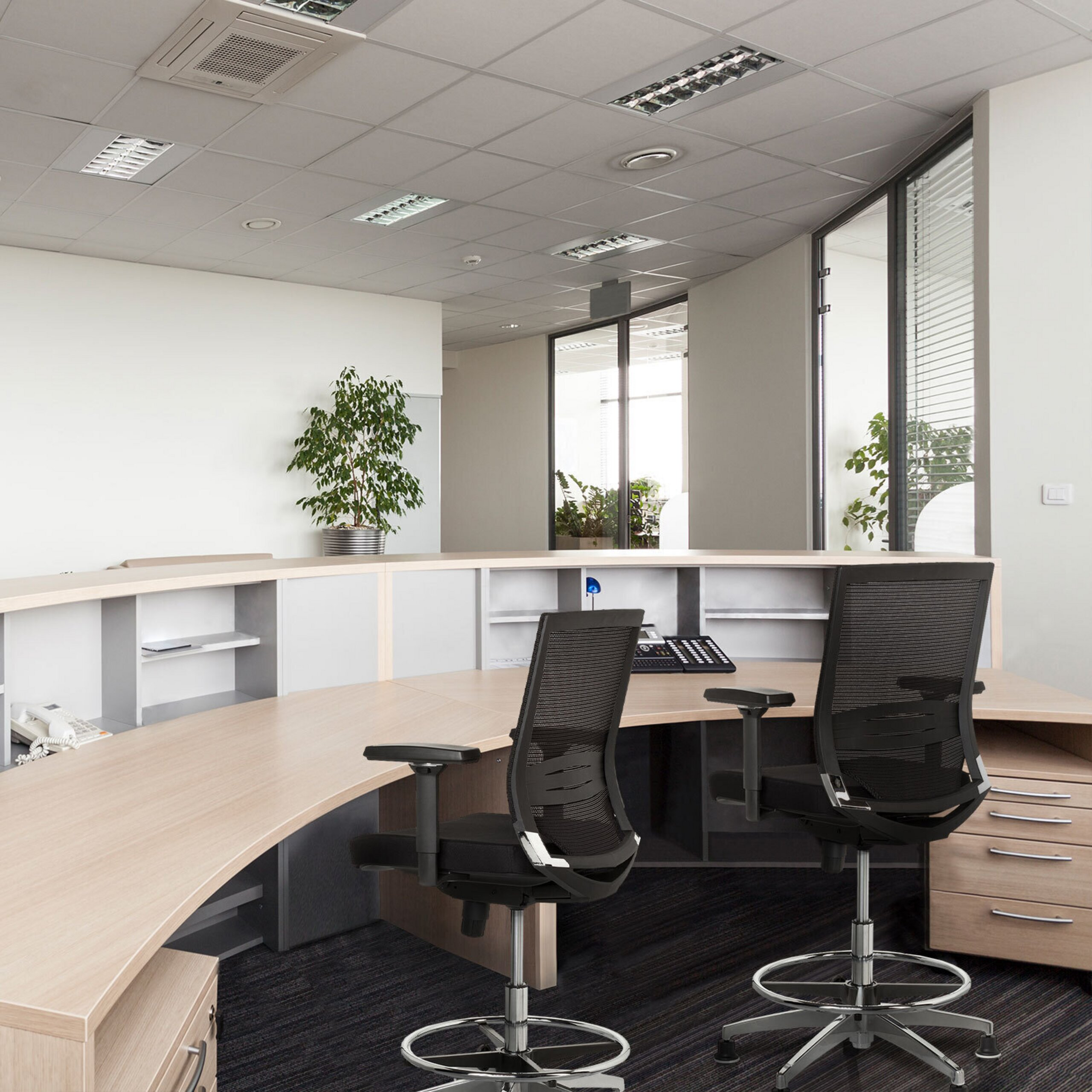 Ein modernes Büro mit einem großen geschwungenen Holztisch und zwei schwarzen Netzstühlen im Vordergrund.