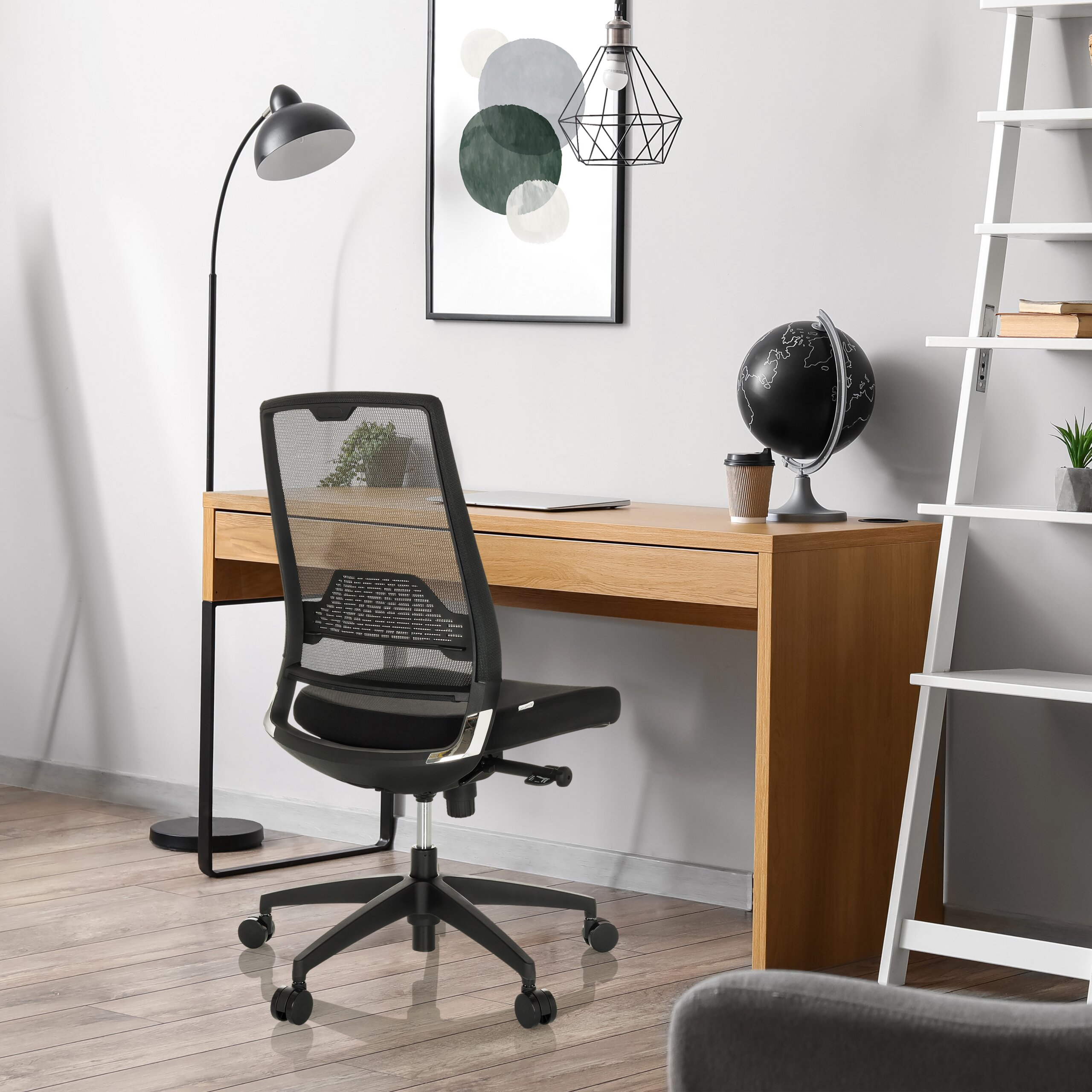Ein modernes Homeoffice mit Holztisch, schwarzem ergonomischem Stuhl, Globus und Kunst an weißer Wand.