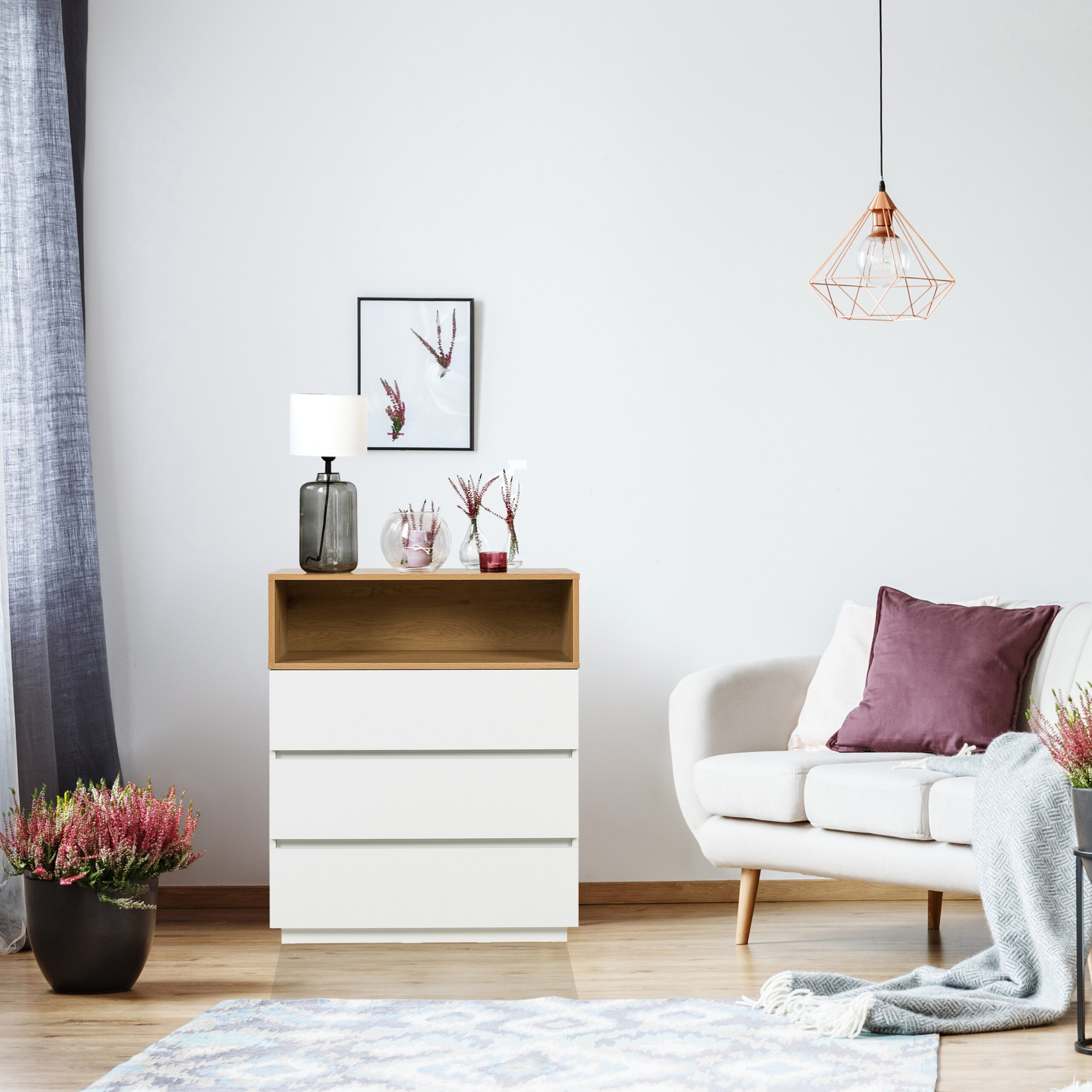 Ein weißer Schrank, ein beiger Sessel mit Kissen, Pflanzen in Töpfen, eine Lampe und eine Deckenleuchte im Raum.