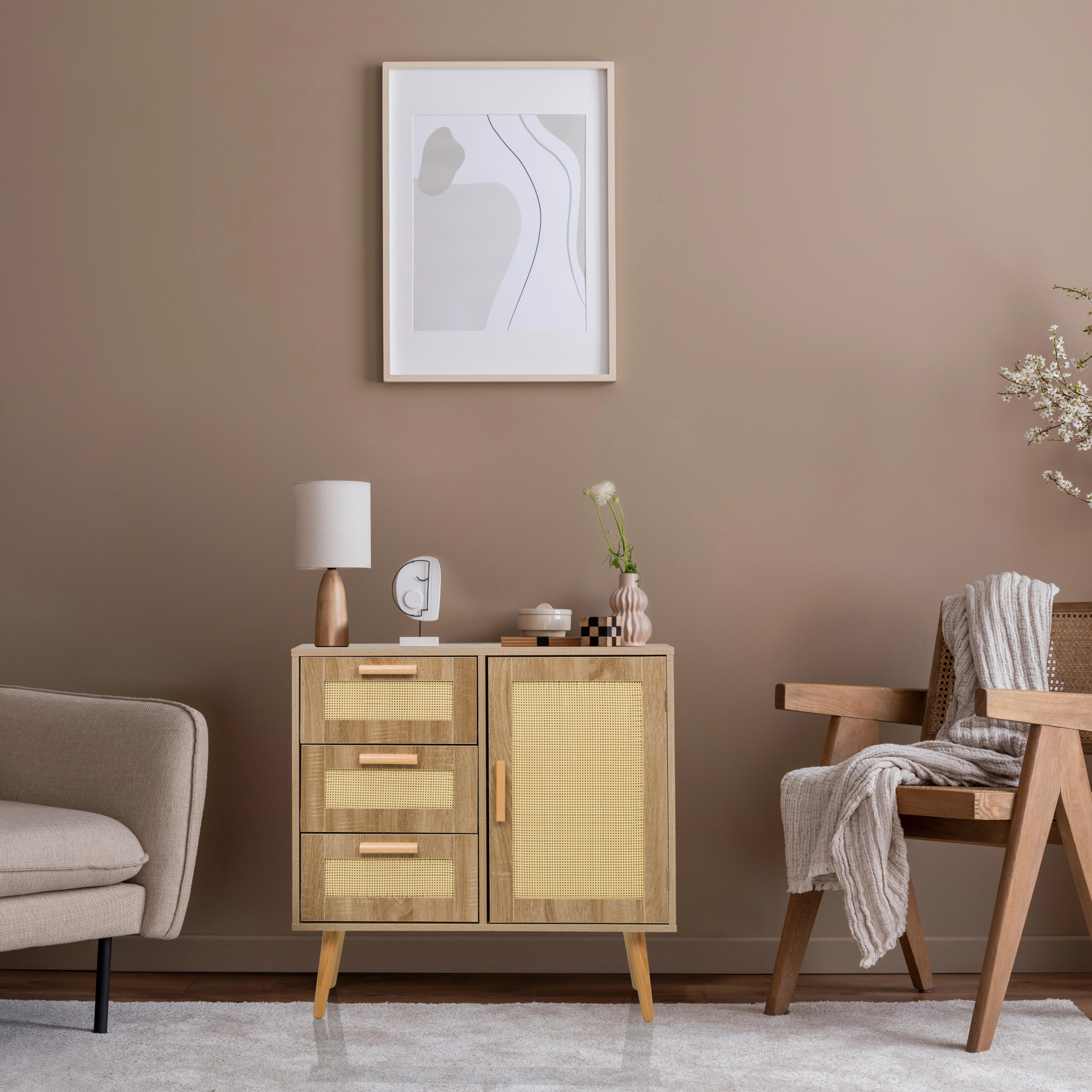 Ein hölzernes Sideboard mit Rattanfronten steht vor einer braunen Wand, flankiert von Sesseln und gerahmter Kunst.