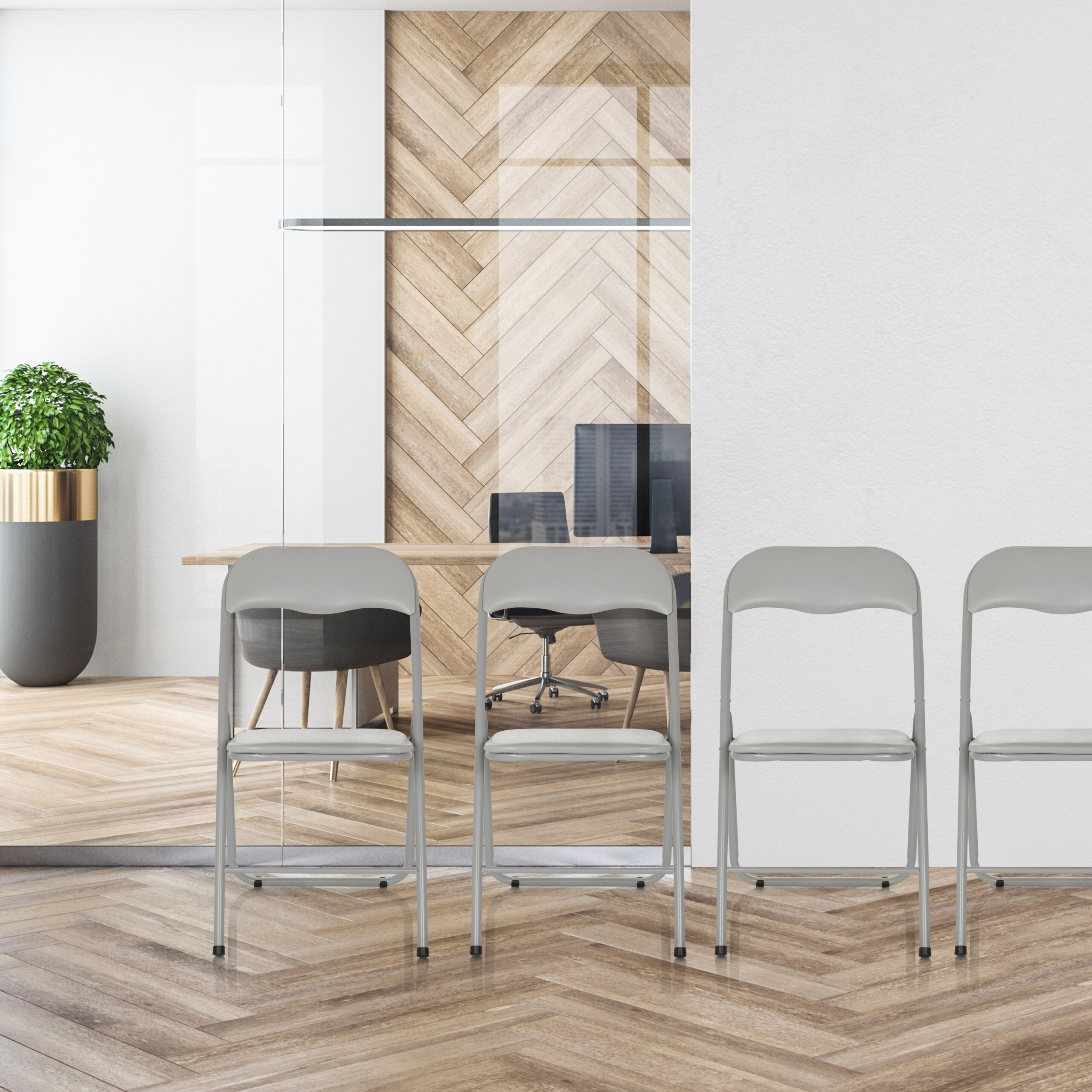Vier graue Klappstühle stehen auf einem Fischgrät-Holzboden vor einem Büro mit Glaswänden.
