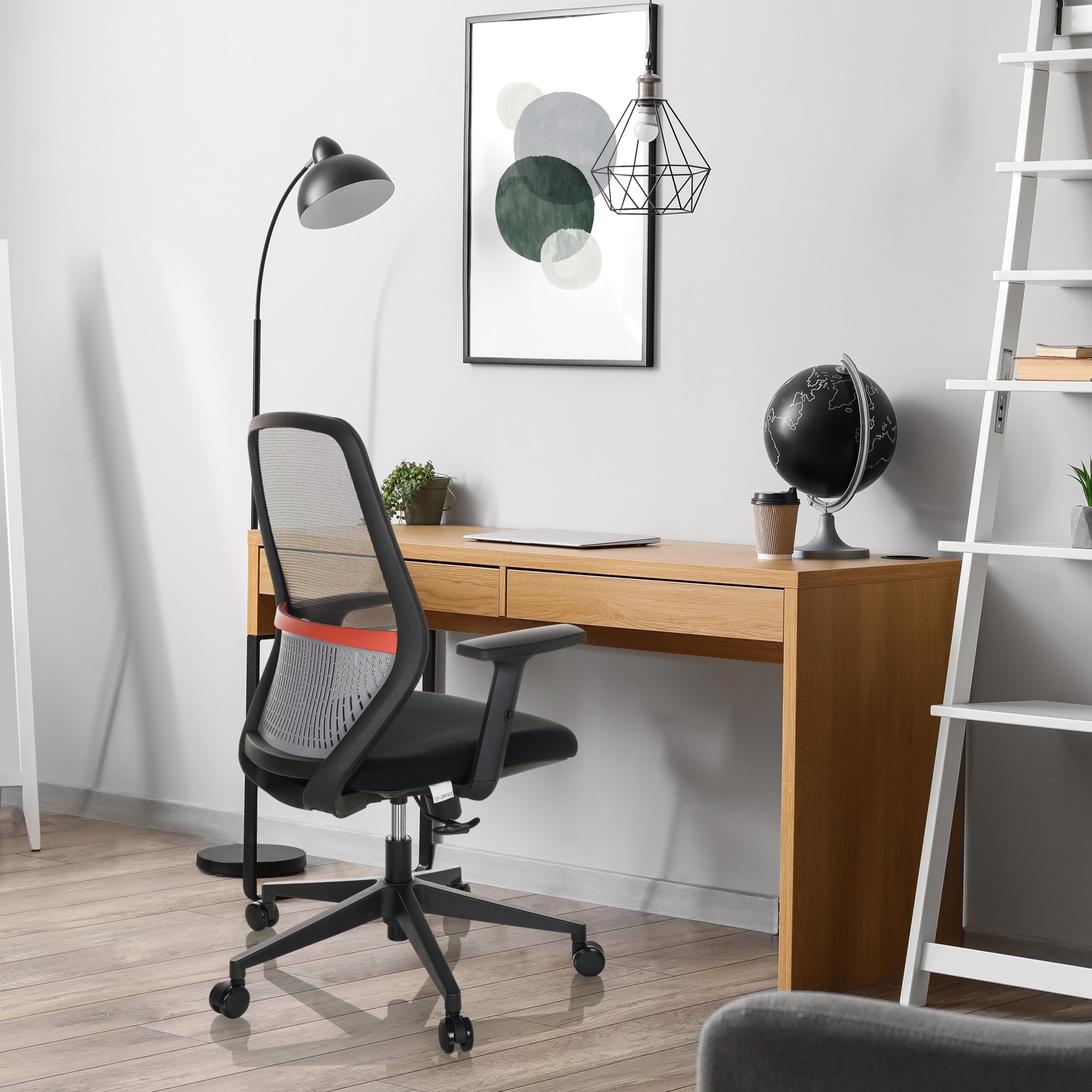 Modernes Heimbüro mit Holztisch, schwarzem Netz-Bürostuhl, Stehlampe, Globus und weißem Leiterregal.