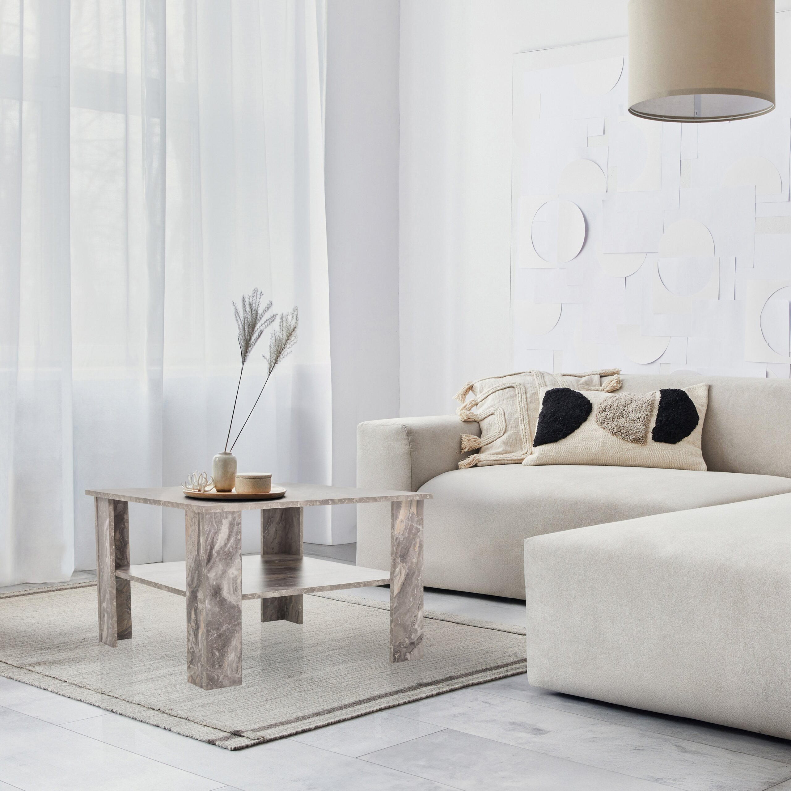 Ein modernes, helles Wohnzimmer mit weißem Sofa, Mamortisch auf Teppich und großen Vorhängen.