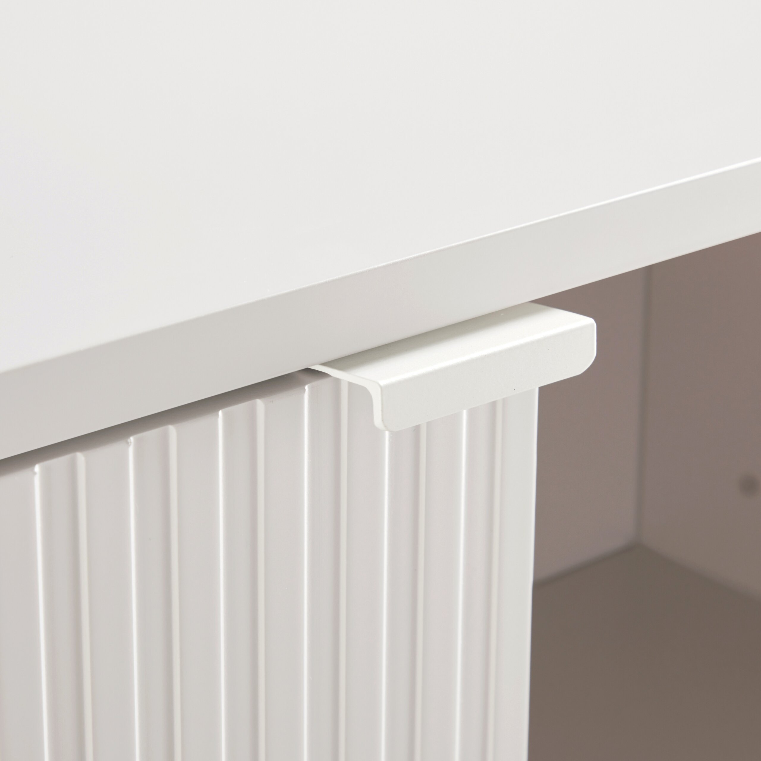 Nahaufnahme einer weißen Möbeloberfläche mit einer gerillten Schubladenfront und einem minimalistischen Griff.