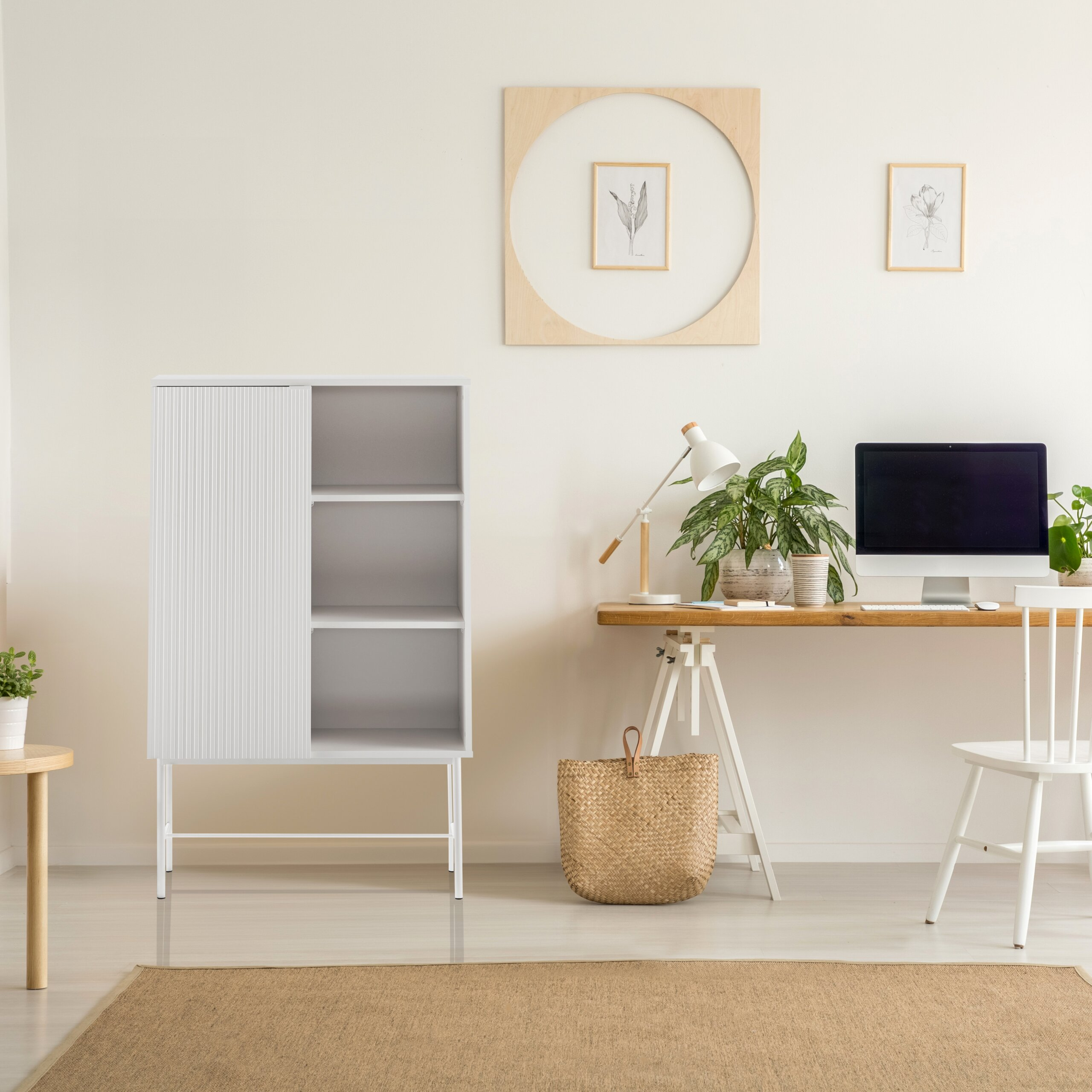 Ein minimalistisches Arbeitszimmer mit weißem Schrank, Holztisch, Computer und Pflanzen vor einer beigen Wand.