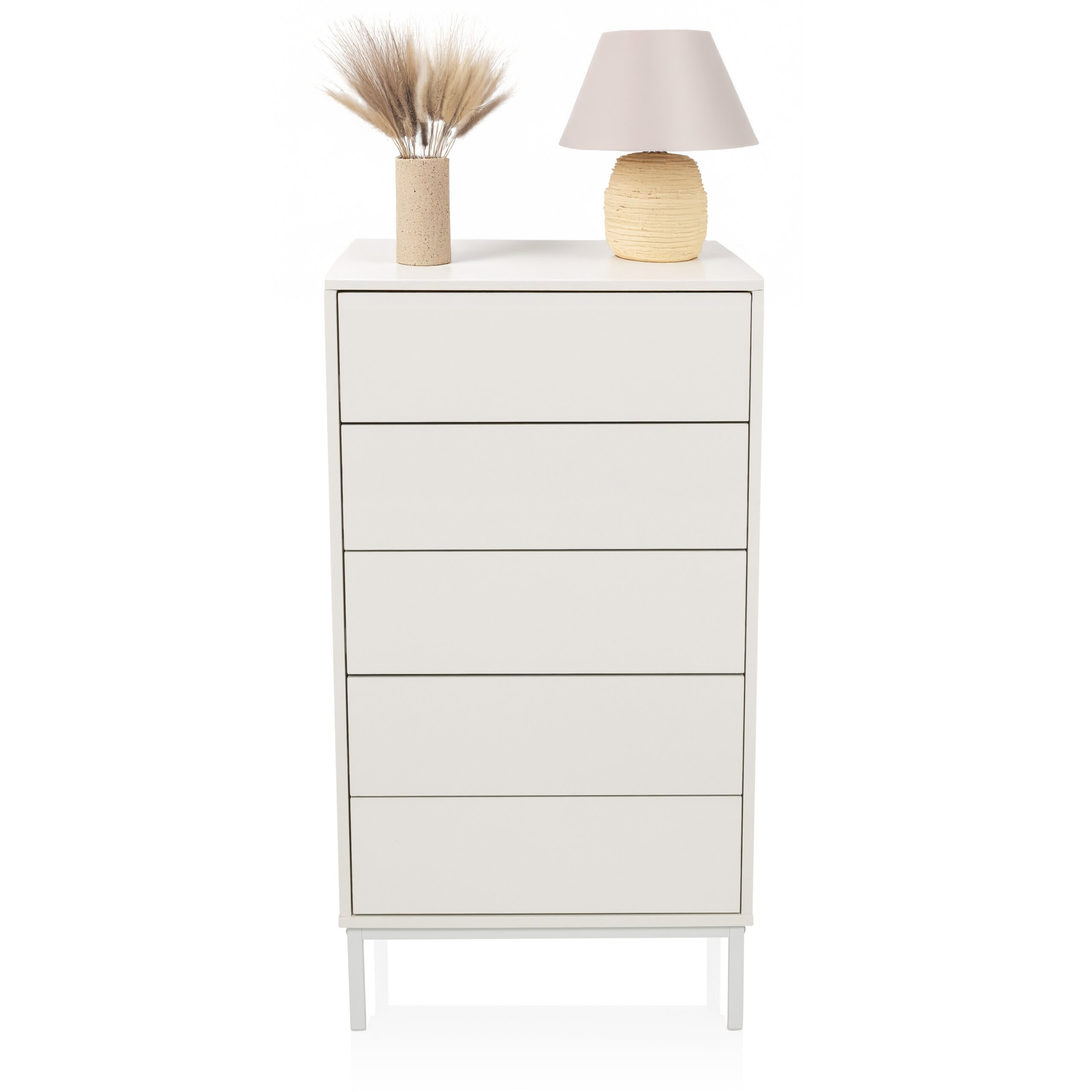 Eine weiße Kommode mit fünf Schubladen, darauf eine Vase mit getrocknetem Gras und eine kleine Tischlampe.