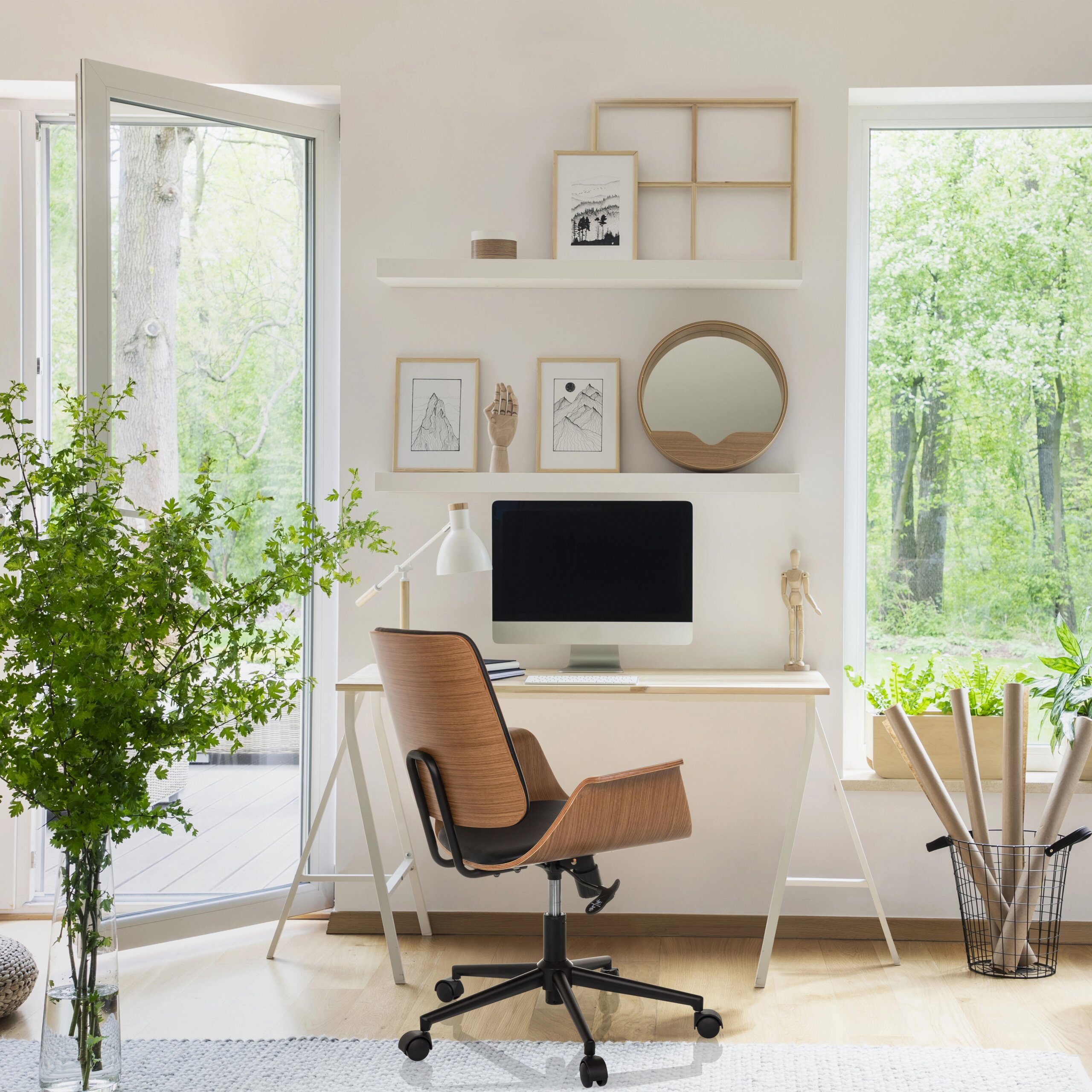 Ein heller Arbeitsplatz mit Computer, Holzstuhl und Wandregalen, flankiert von großen Fenstern ins Grüne.