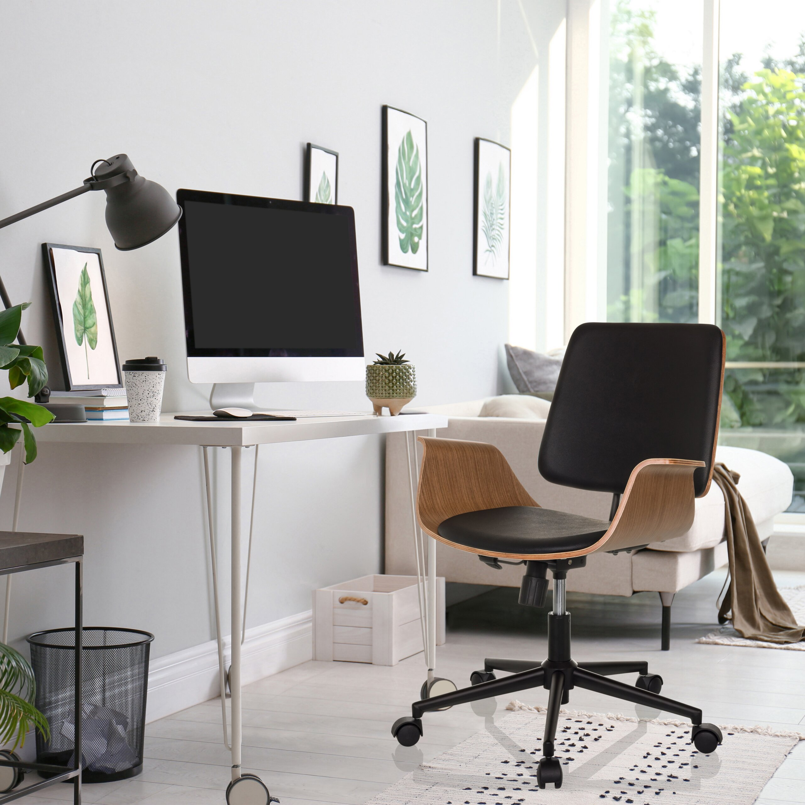 Modernes Arbeitszimmer mit weißem Schreibtisch, Computer, schwarzem Stuhl und großen Fenstern mit grünem Ausblick.