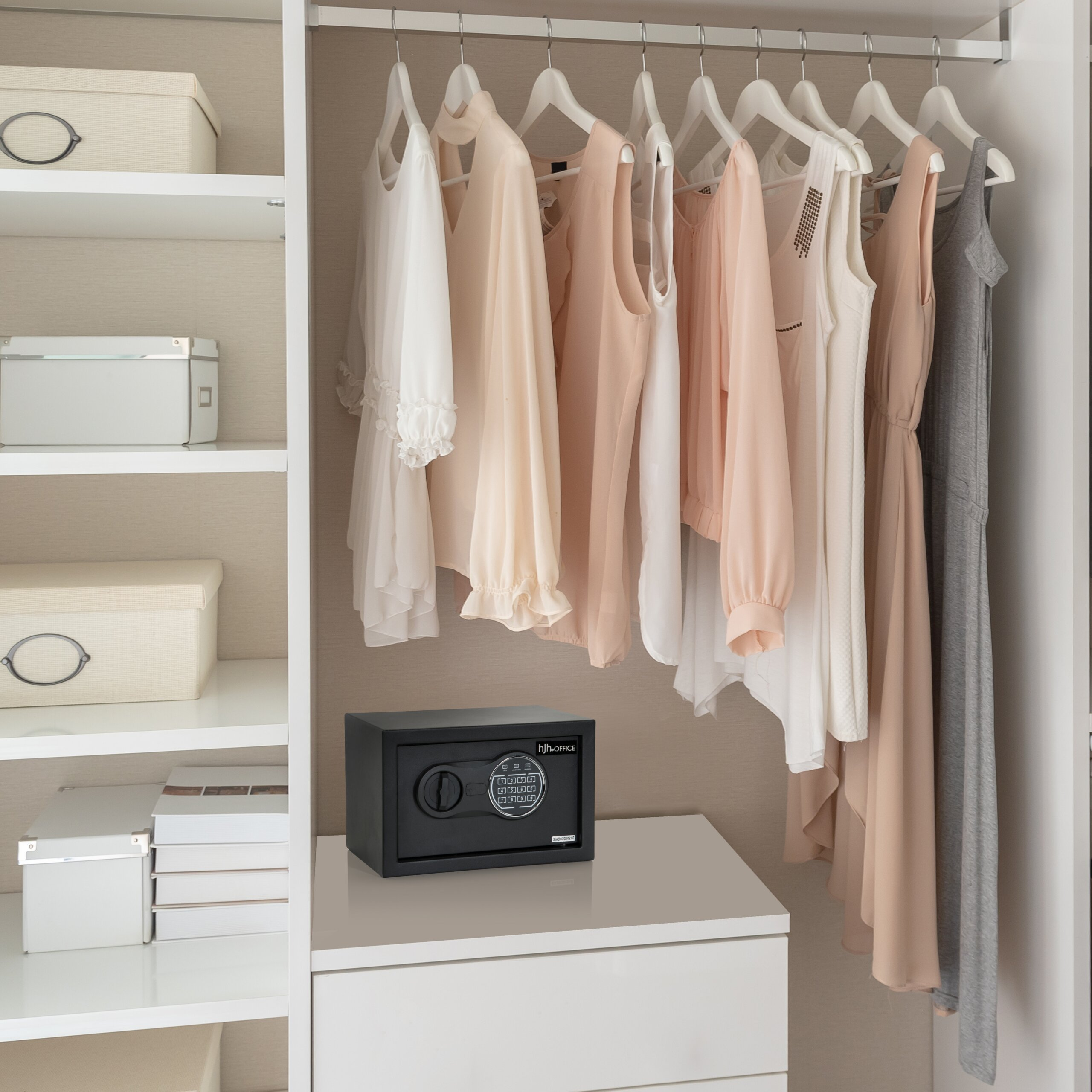 Ein weißer Kleiderschrank mit Pastellkleidung, Boxen auf Regalen und einem schwarzen Safe unten.