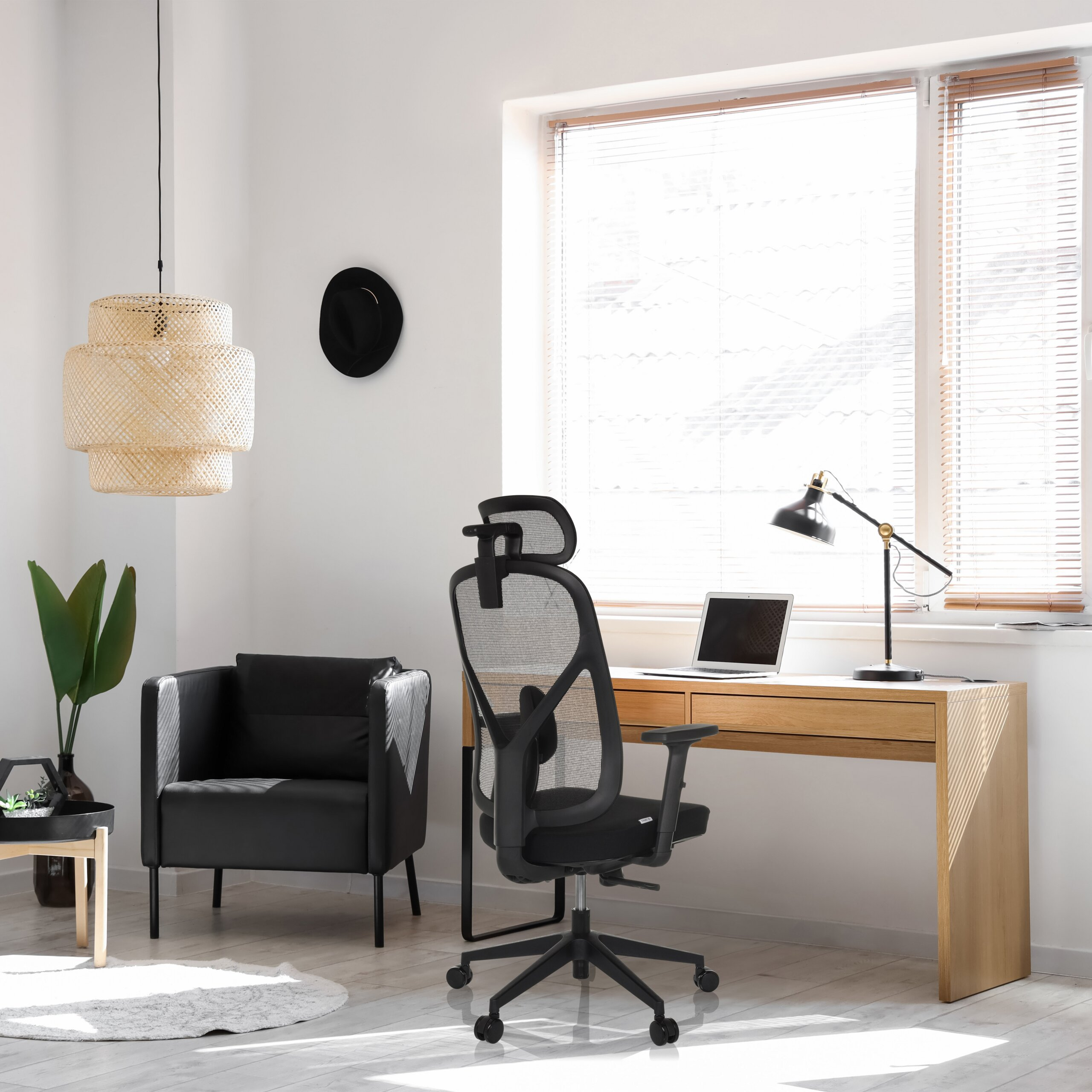 Büro mit Holztisch, schwarzem Chefsessel, Sessel, Lampe und grossem Fenster mit Jalousien.