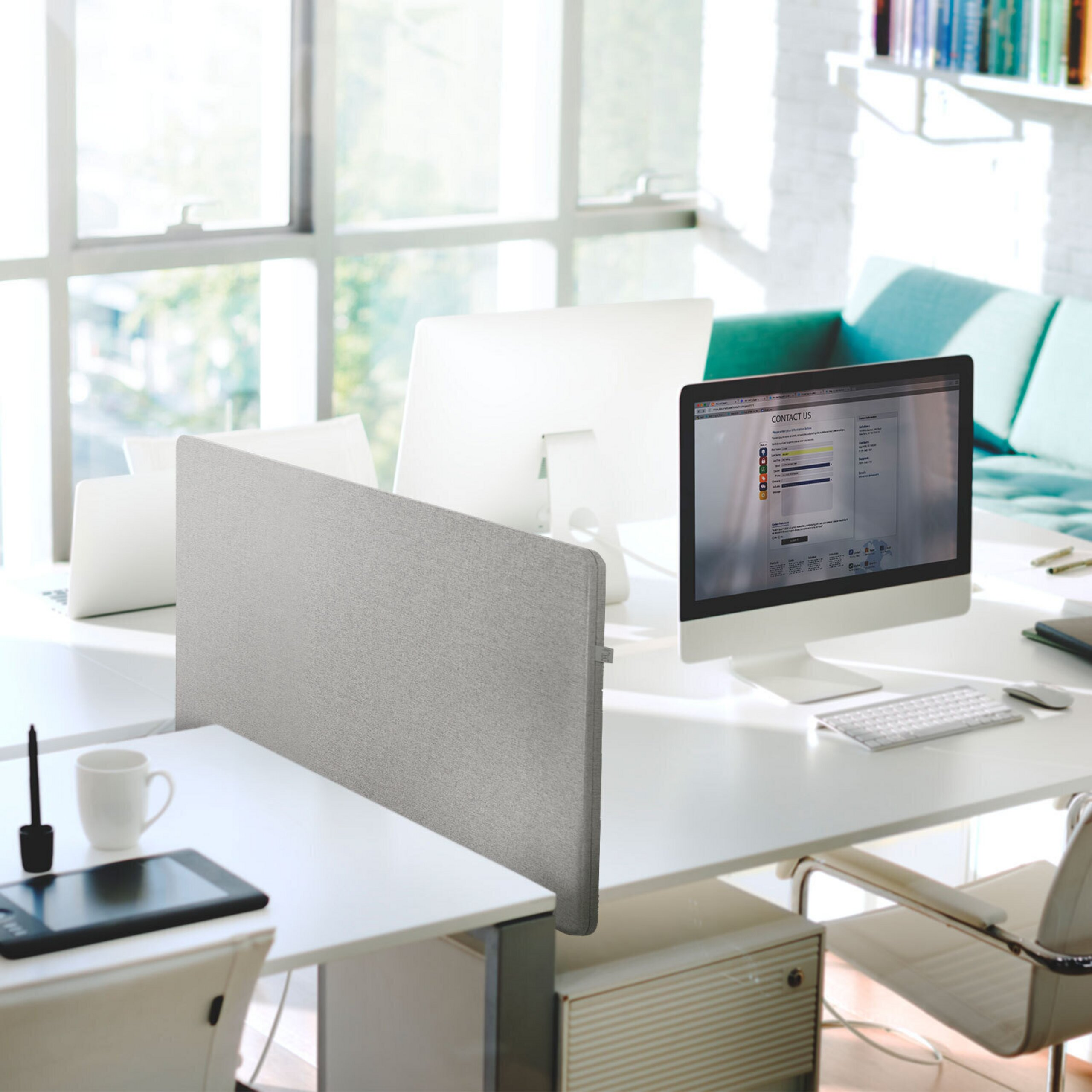 Helles modernes Büro mit weißen Schreibtischen, Computern, grauen Sichtschutzwänden und einem türkisfarbenen Sofa.