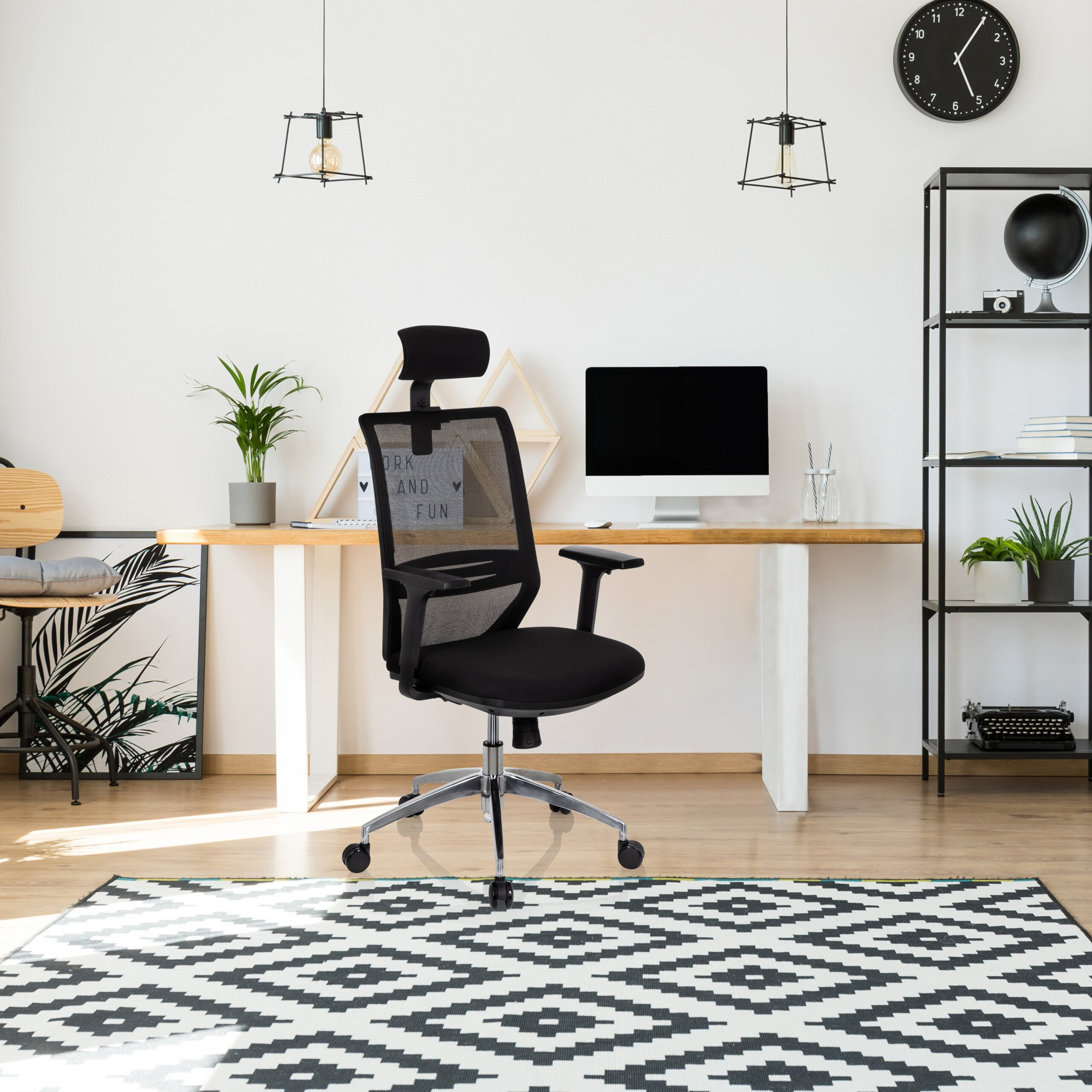 Moderner Büroarbeitsplatz mit schwarzem Bürostuhl, Holztisch, Computer, Regal und Teppich mit geometrischem Muster.