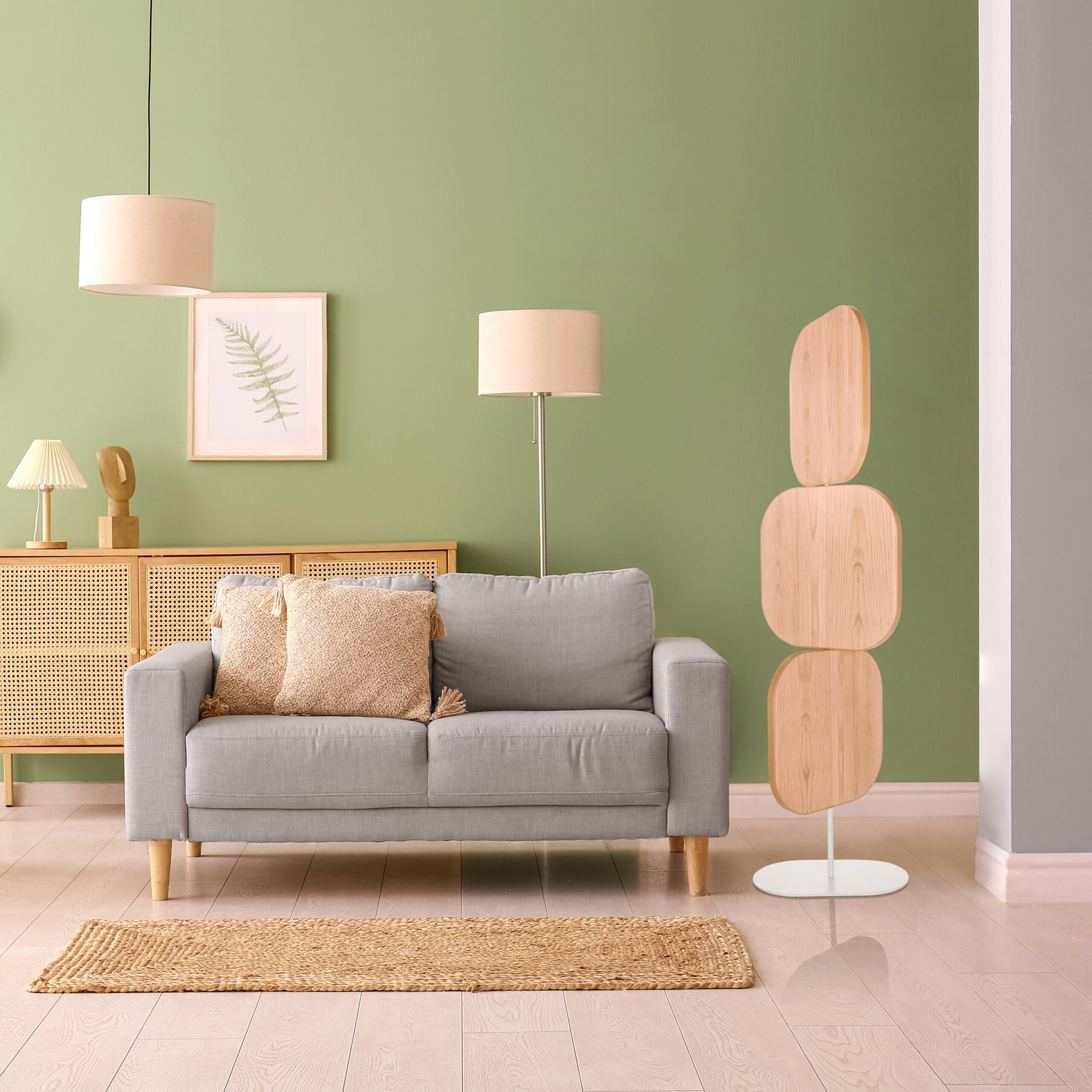 Ein graues Sofa mit Kissen steht vor einer grünen Wand, neben einem Holzschrank und dekorativen Lampen.